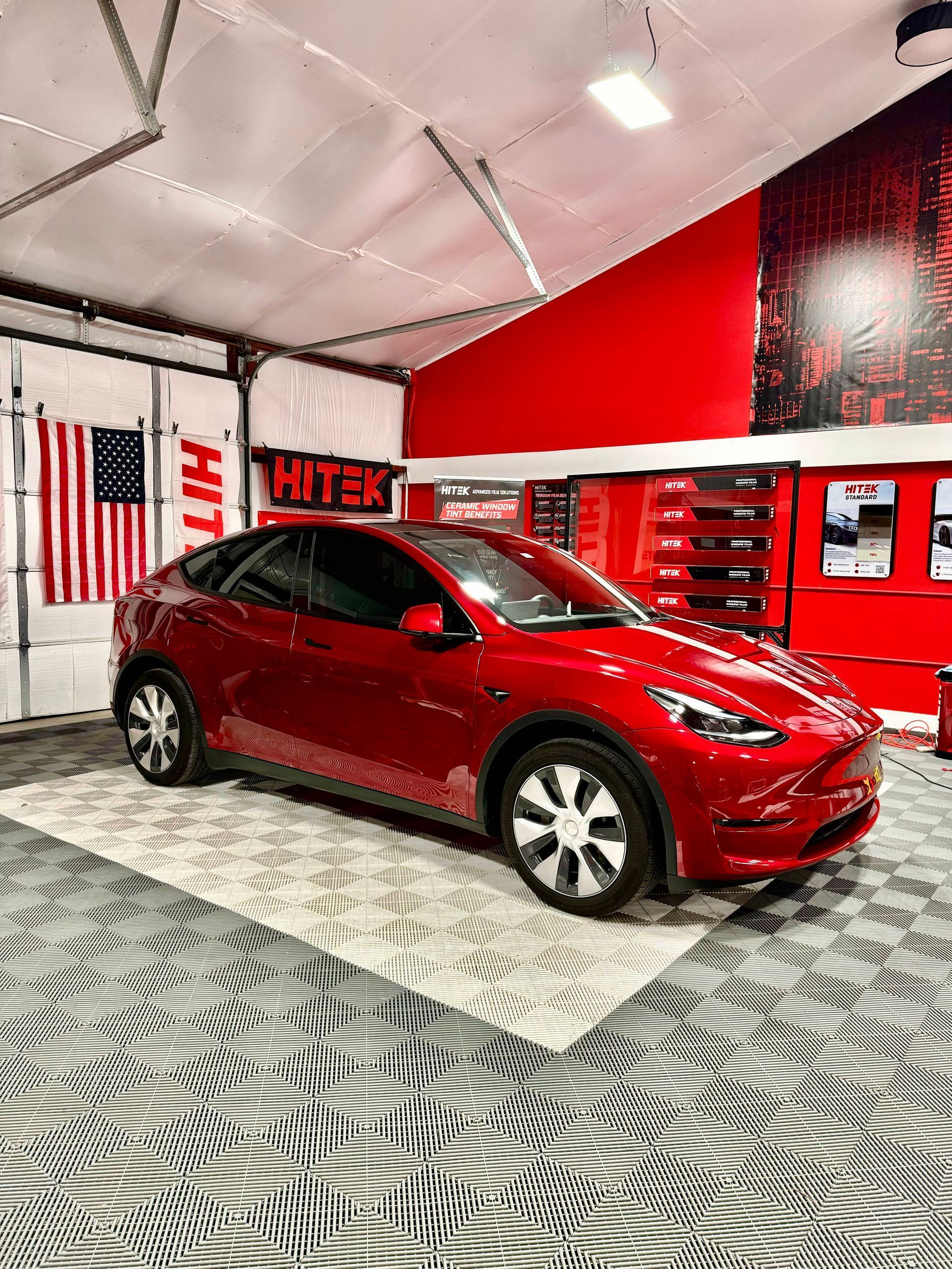 Red Tesla Model Y inside a garage with American flag, gray and white flooring, and red accents.