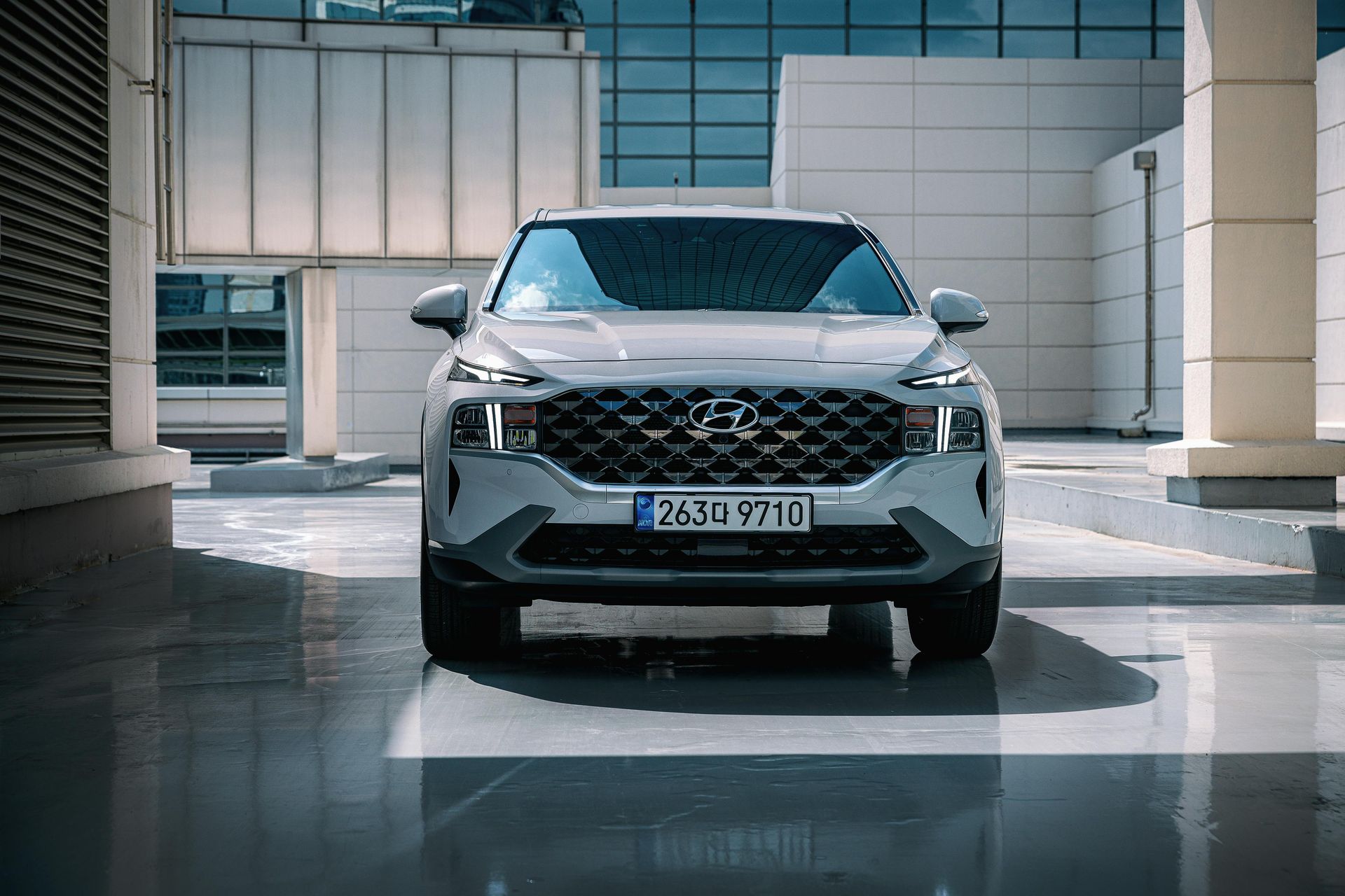 Silver Hyundai Santa Fe SUV parked in front of a modern building with reflections on a wet ground.