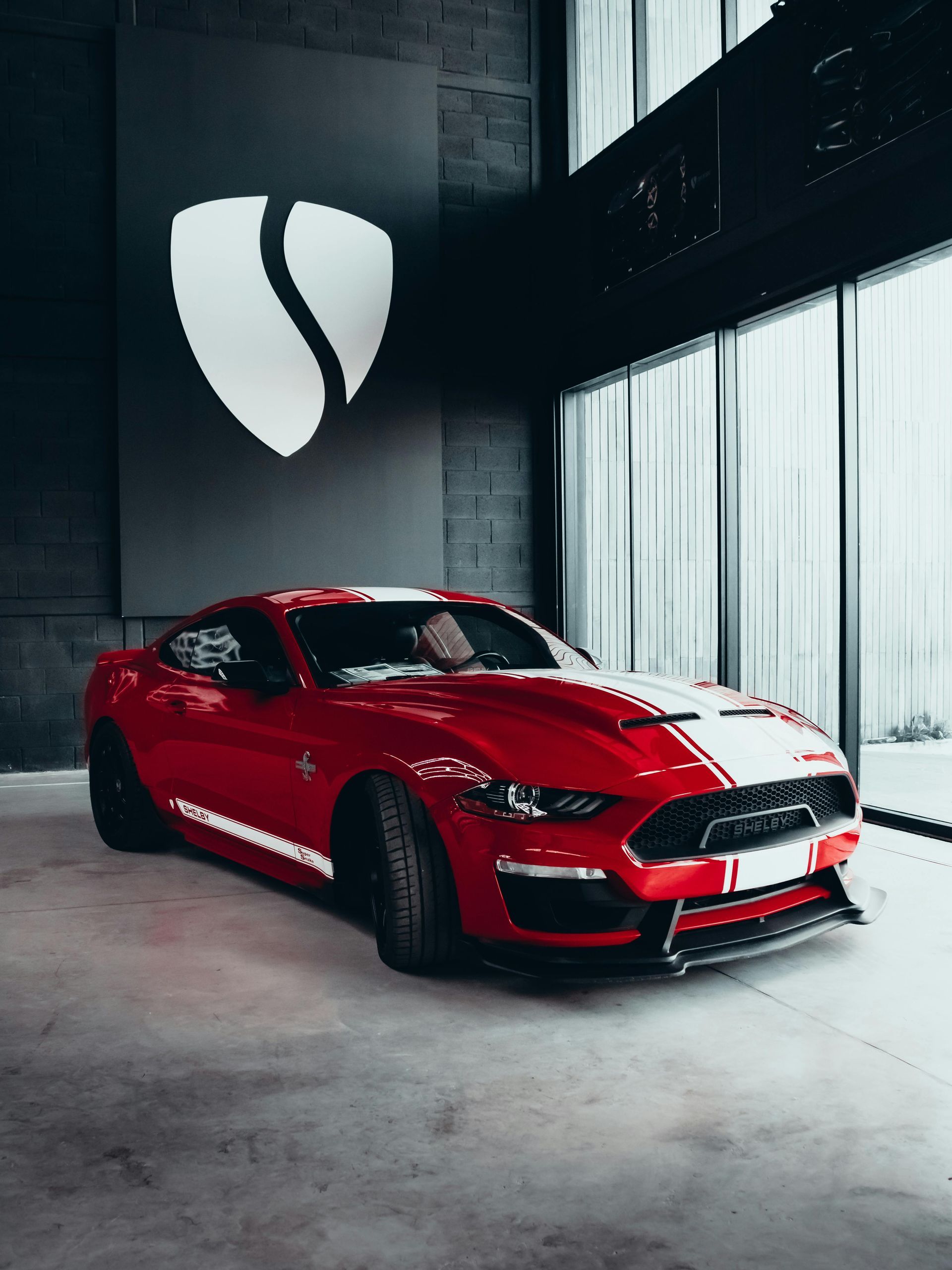 Red Ford Mustang in a modern showroom with a logo on the wall.