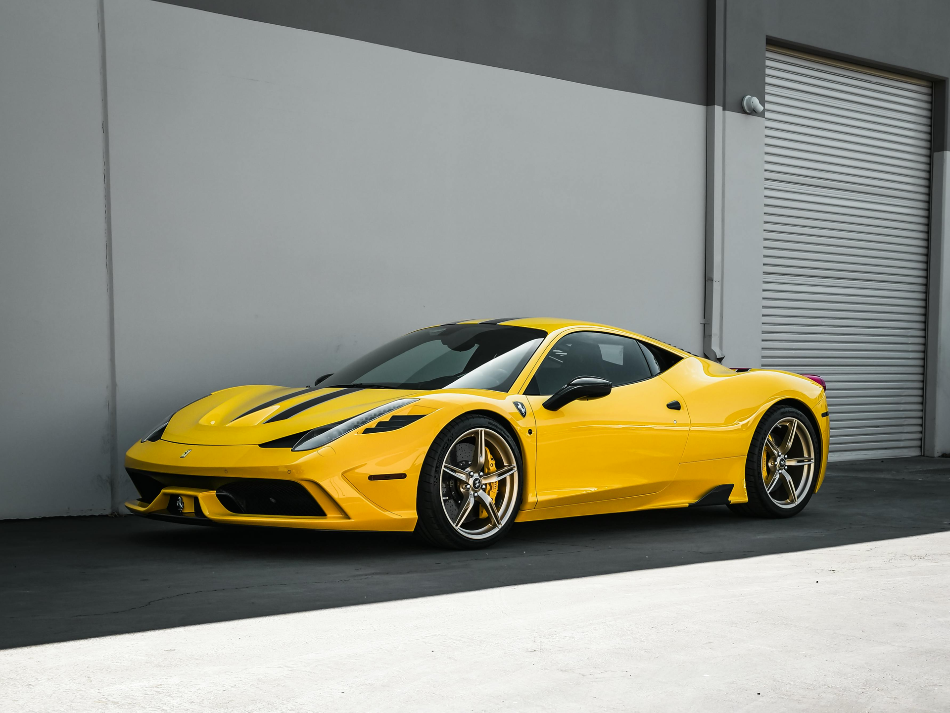 Yellow sports car parked outside a building with a gray wall and garage door.