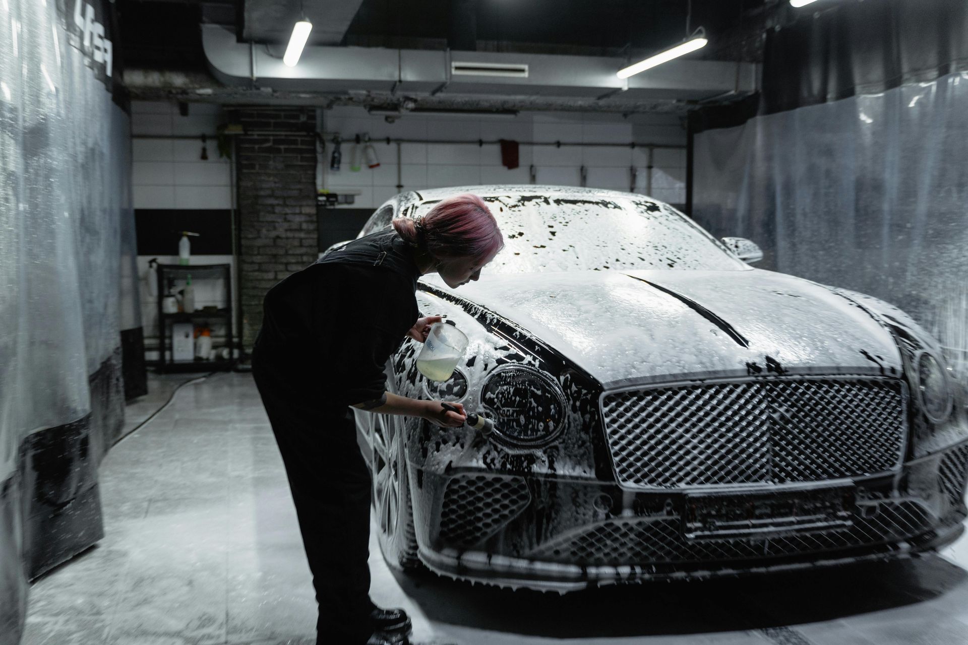 Person washing a Bentley with soapy foam in a car wash setting.