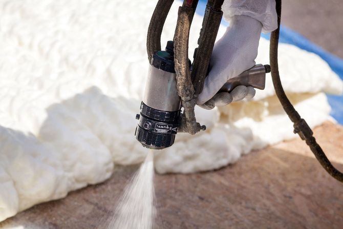 Close up of spray foam insulation nozzle applying foam to flooring.