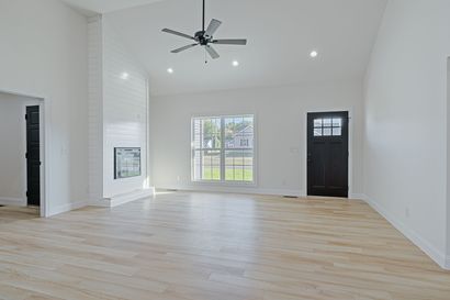 A kitchen with white cabinets , wooden floors , stainless steel appliances and a large island with chairs.