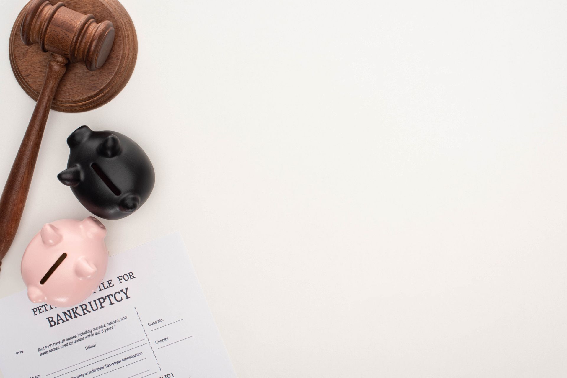 Wooden gavel, pink and black piggy banks, and a bankruptcy form on a white surface.