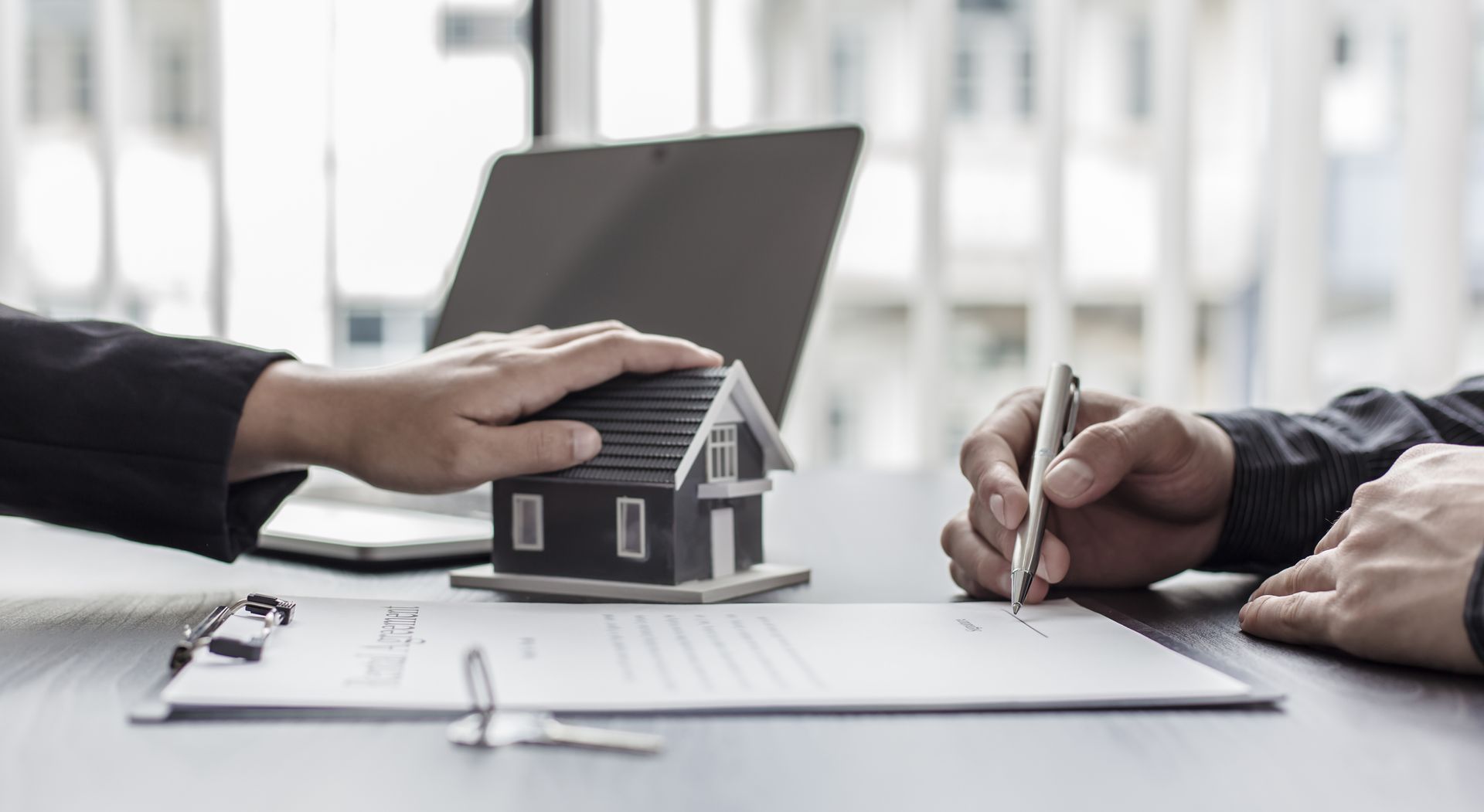 A man is holding a model house while another man signs a document.