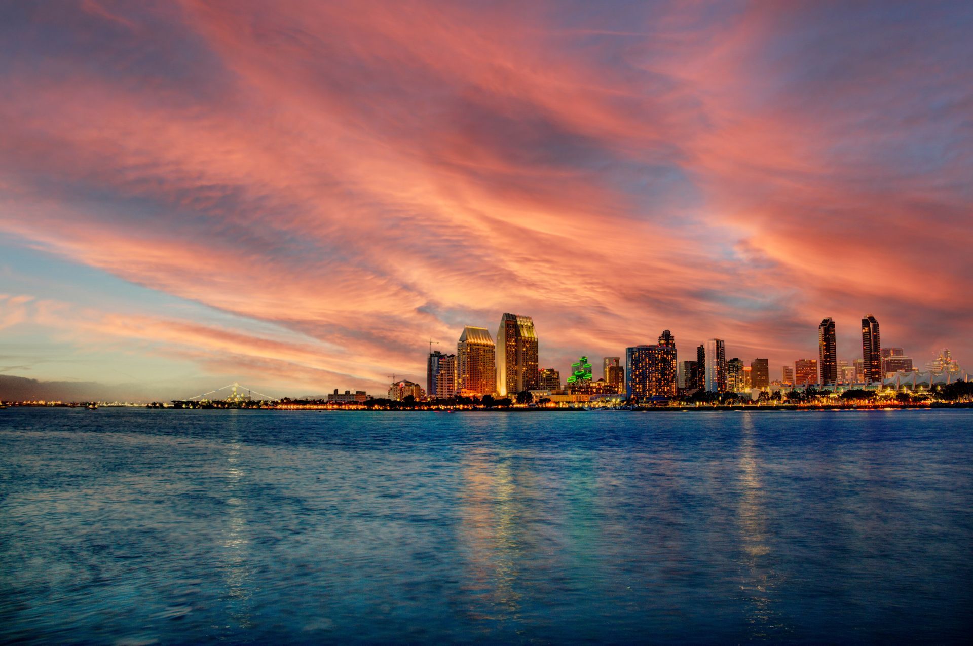 The skyline of san diego is reflected in the water at sunset.
