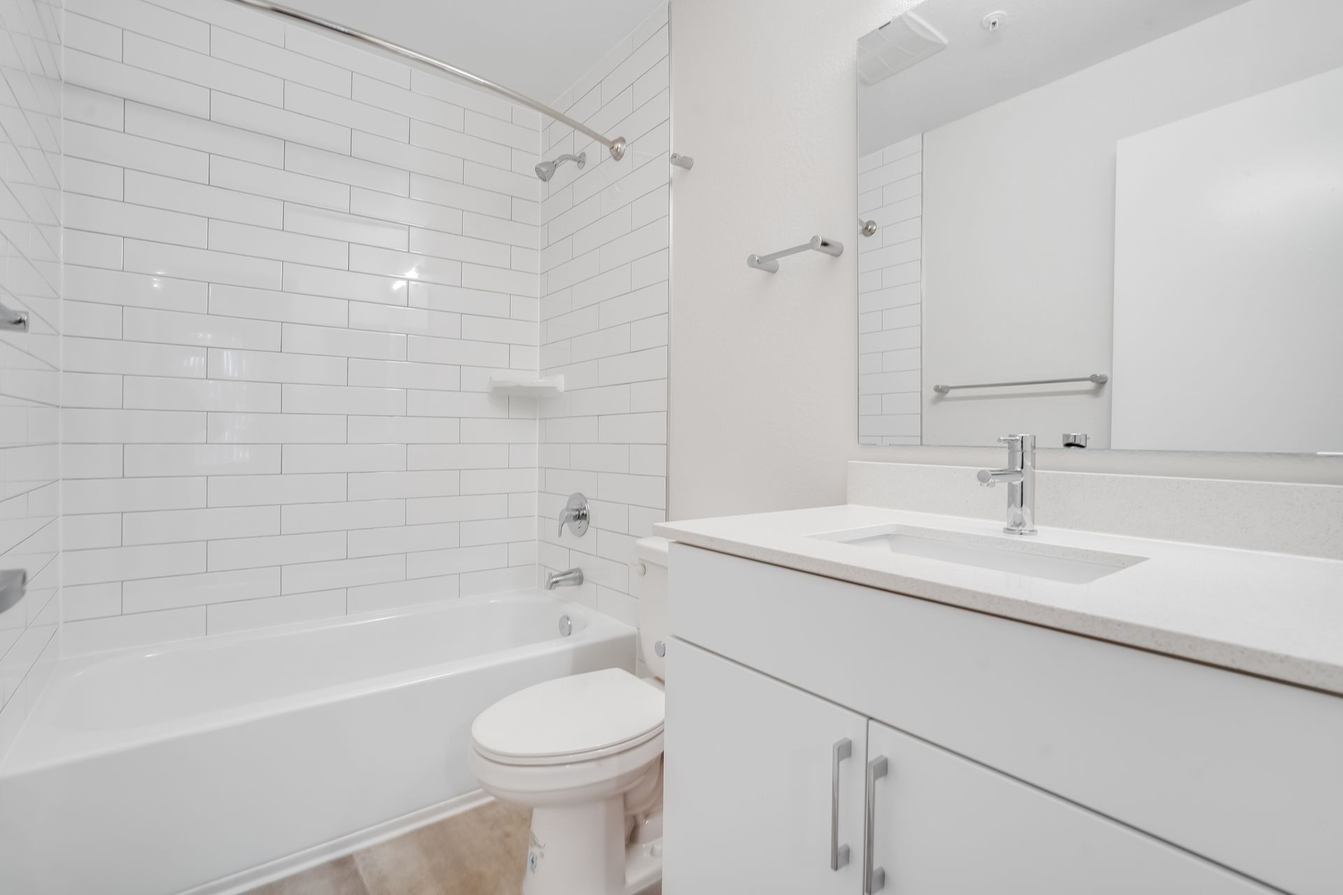 White bathroom with a tub, toilet, vanity, and large mirror.