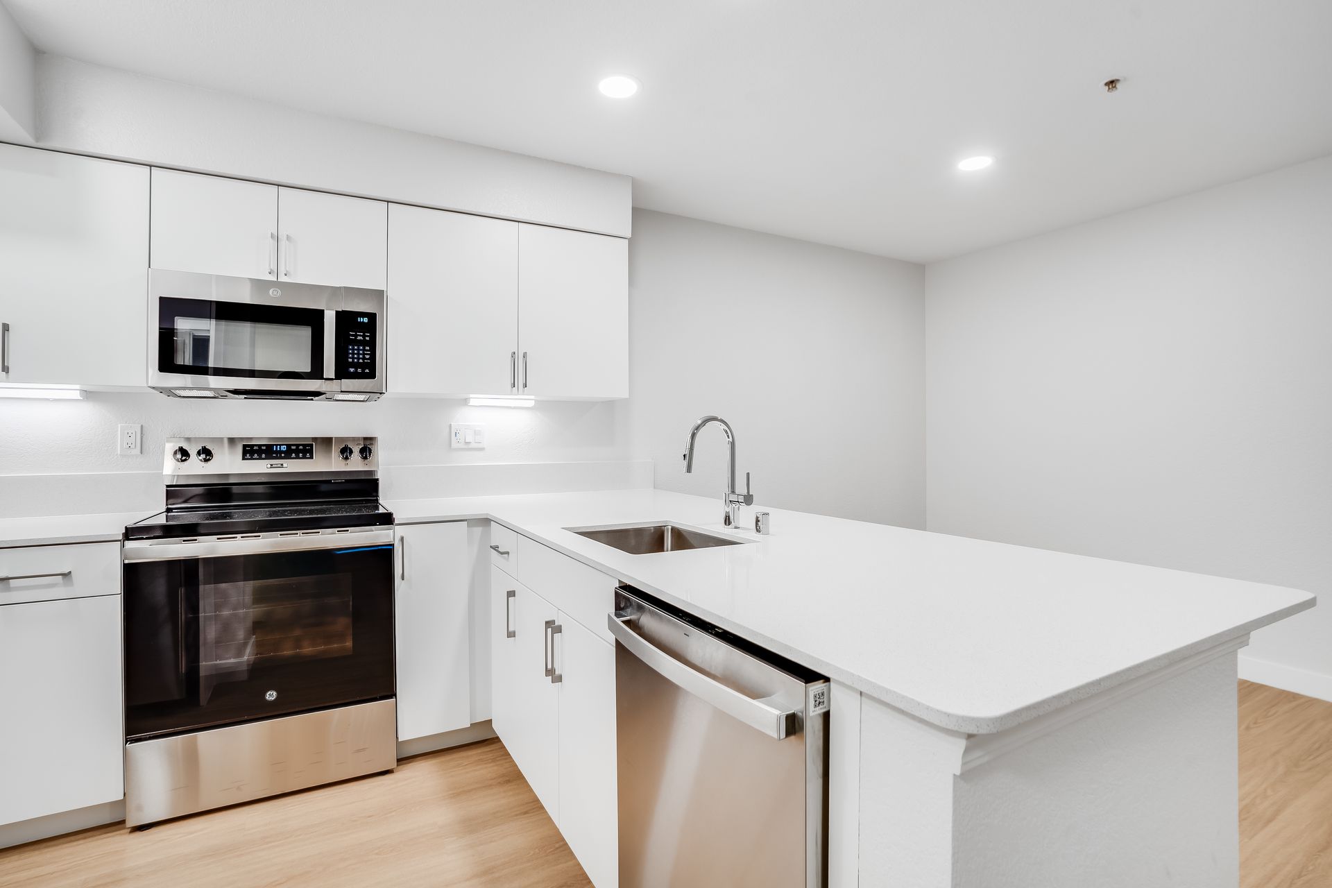 Modern white kitchen with stainless steel appliances, island, and wood floors.
