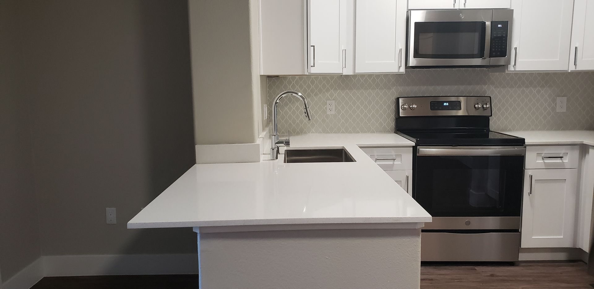 Modern white kitchen with island, stainless steel appliances, and gray walls.