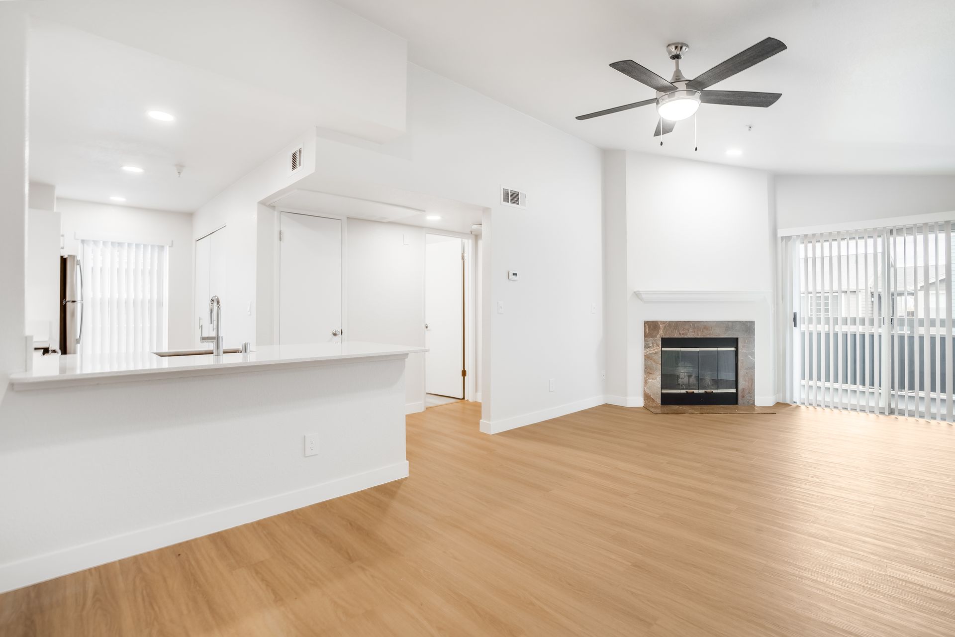 Open-concept living space with white walls, light wood floors, fireplace, and sliding glass doors.