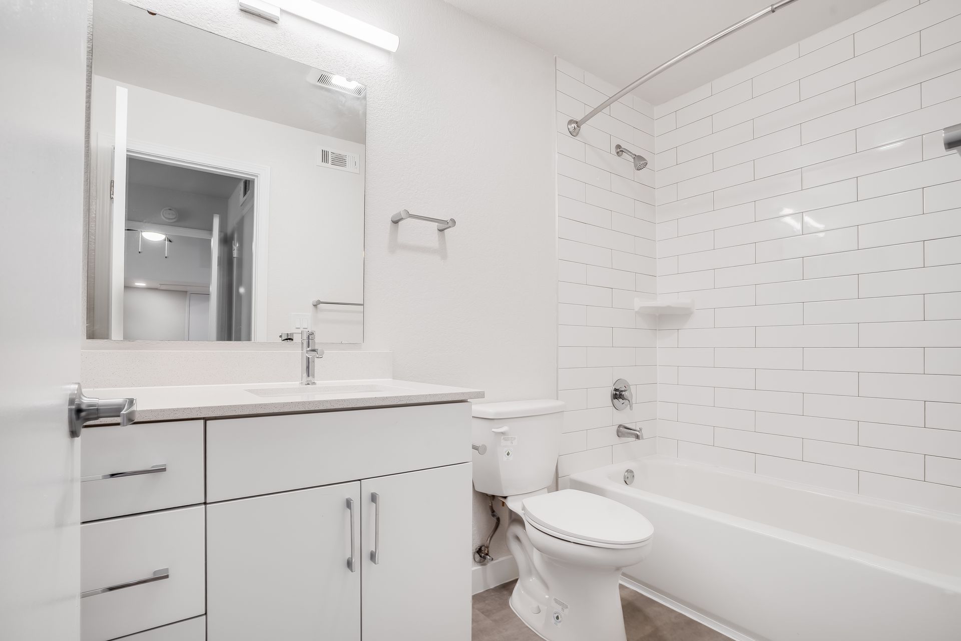 White bathroom with a vanity, toilet, and bathtub with tiled wall.