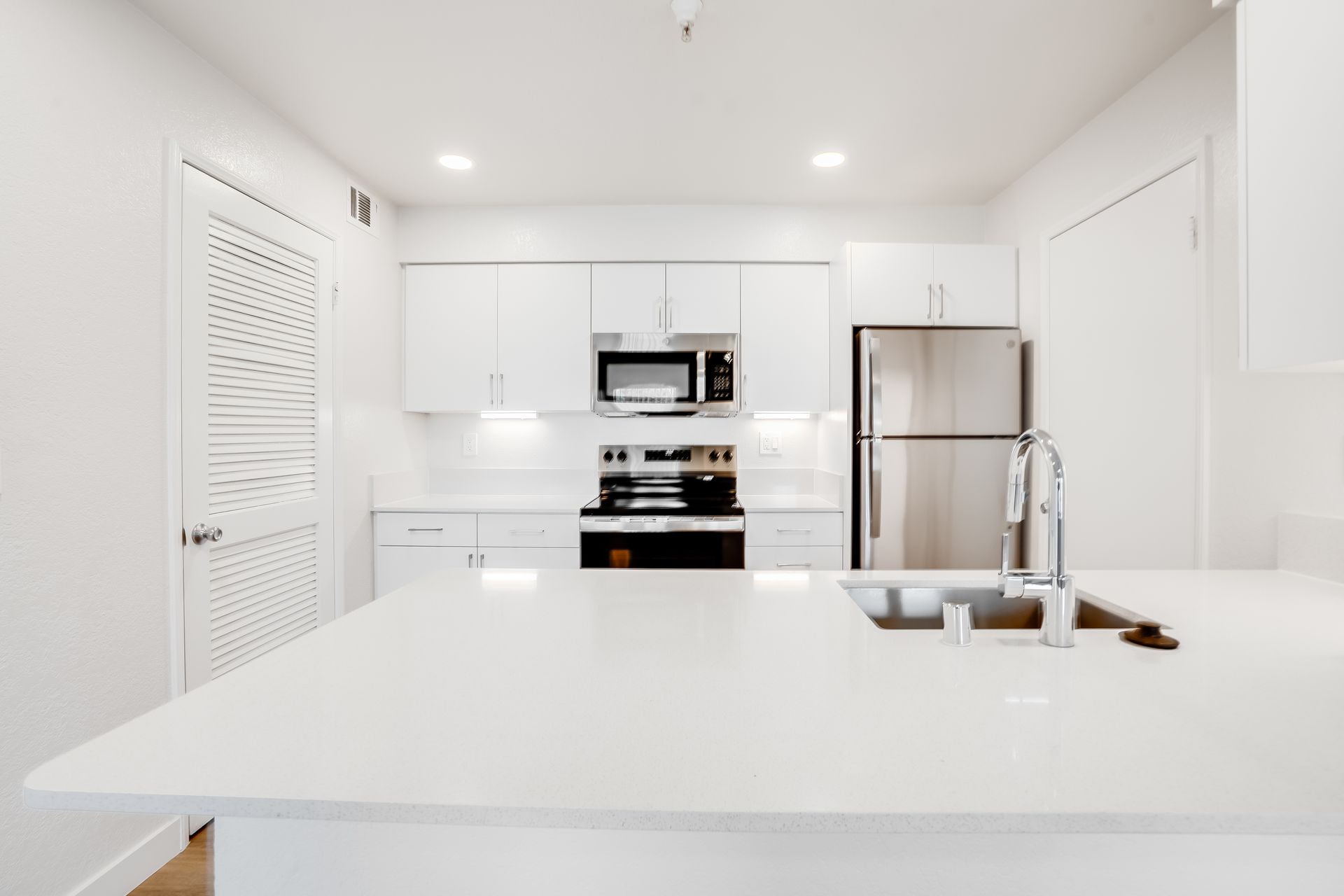 Bright white kitchen with stainless steel appliances. White cabinets, countertops, and an island.
