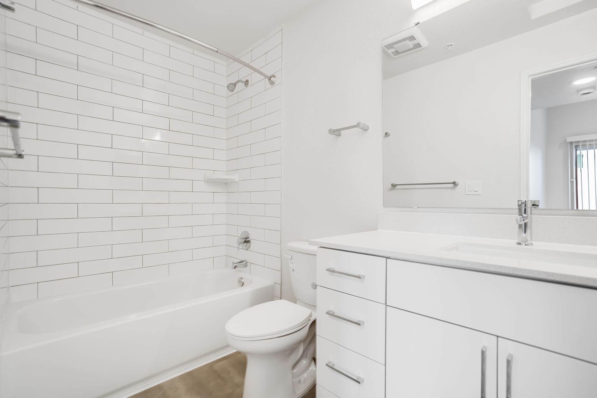 White bathroom with a tub, toilet, and vanity. Subway tile and silver fixtures.