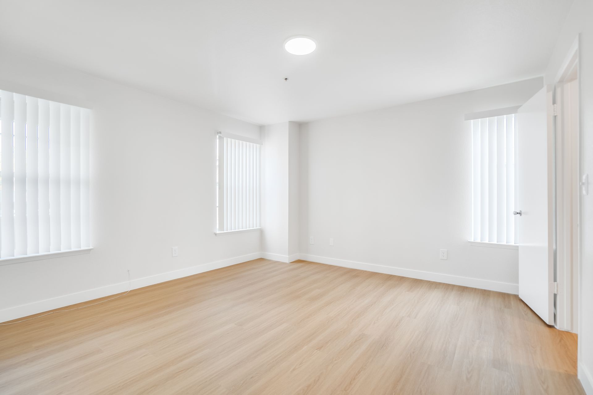 Empty, bright white room with three windows and light wood floors.