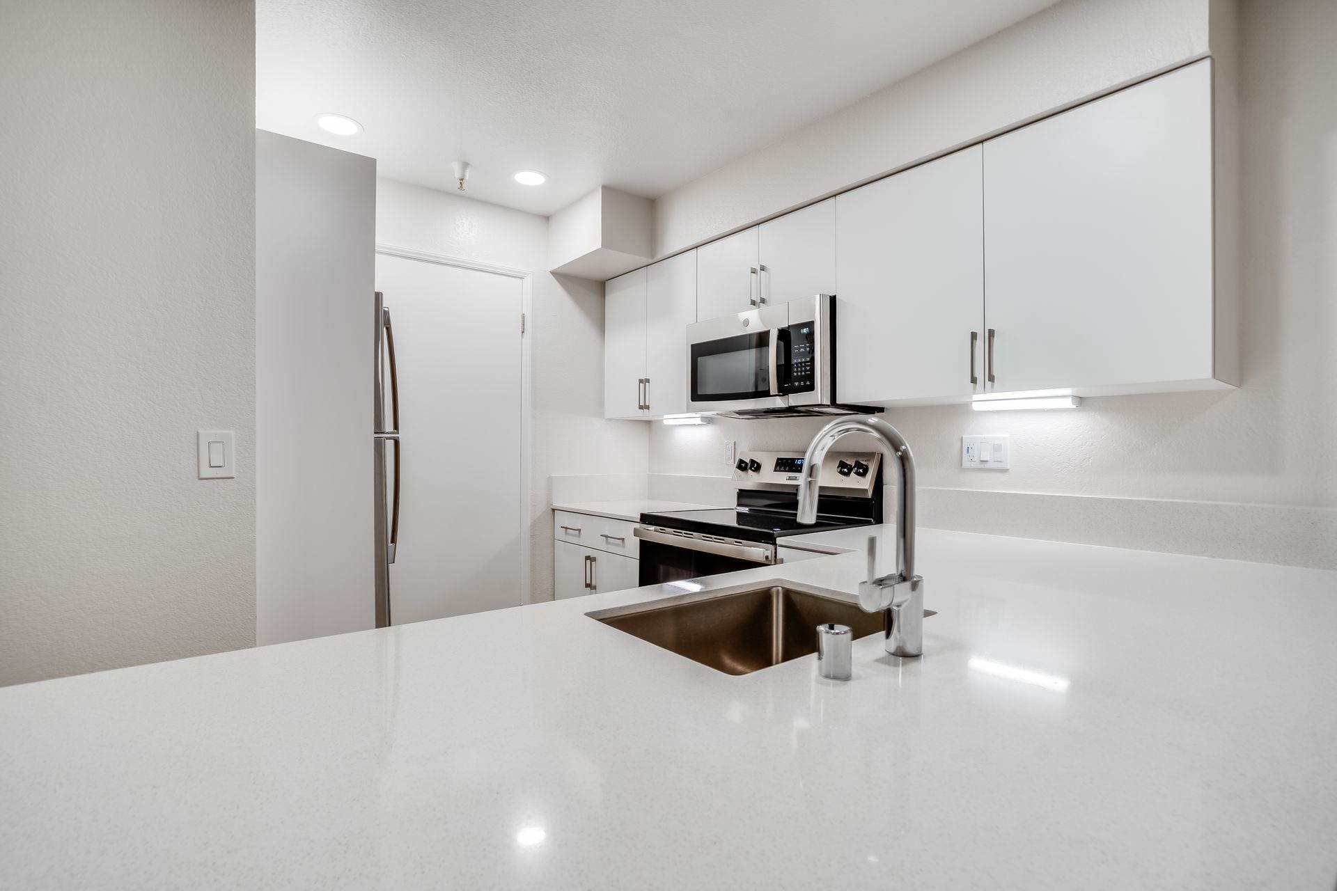 Modern kitchen with white cabinets, countertops, and stainless steel appliances.