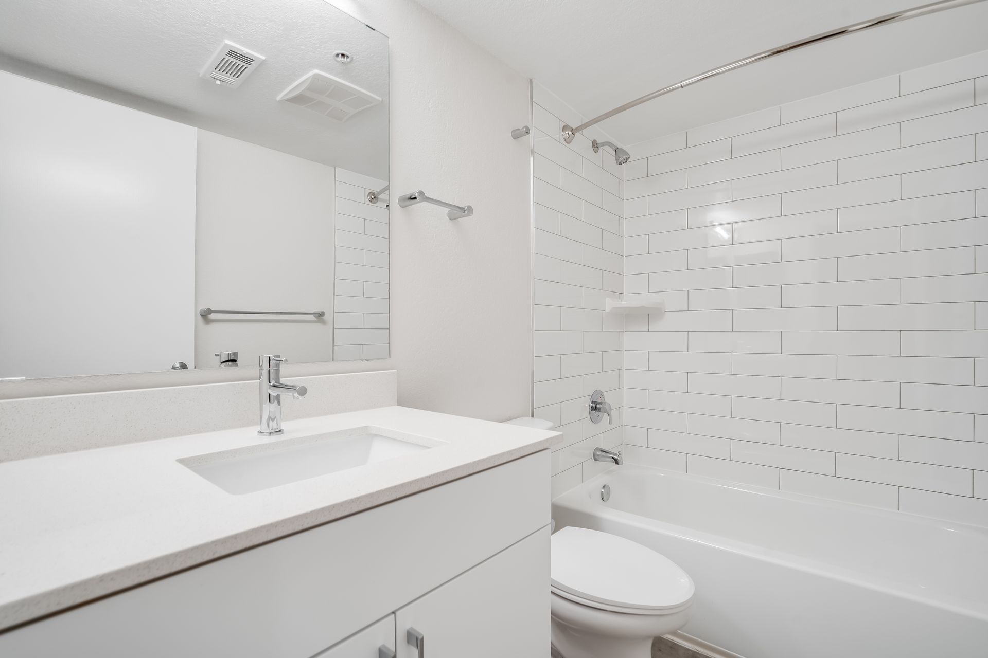 White bathroom with a sink, toilet, and bathtub with white subway tile.