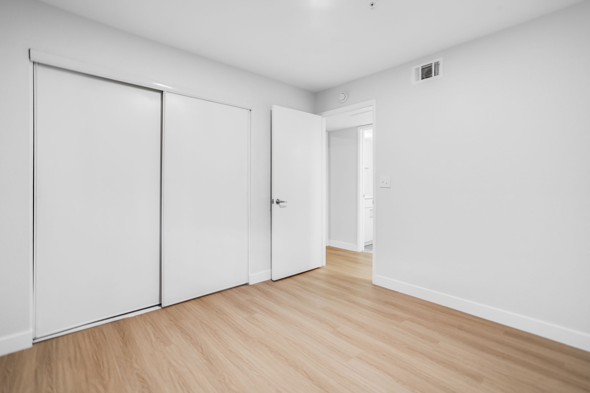 Empty bedroom with white walls, closet, door, and wood-look flooring.