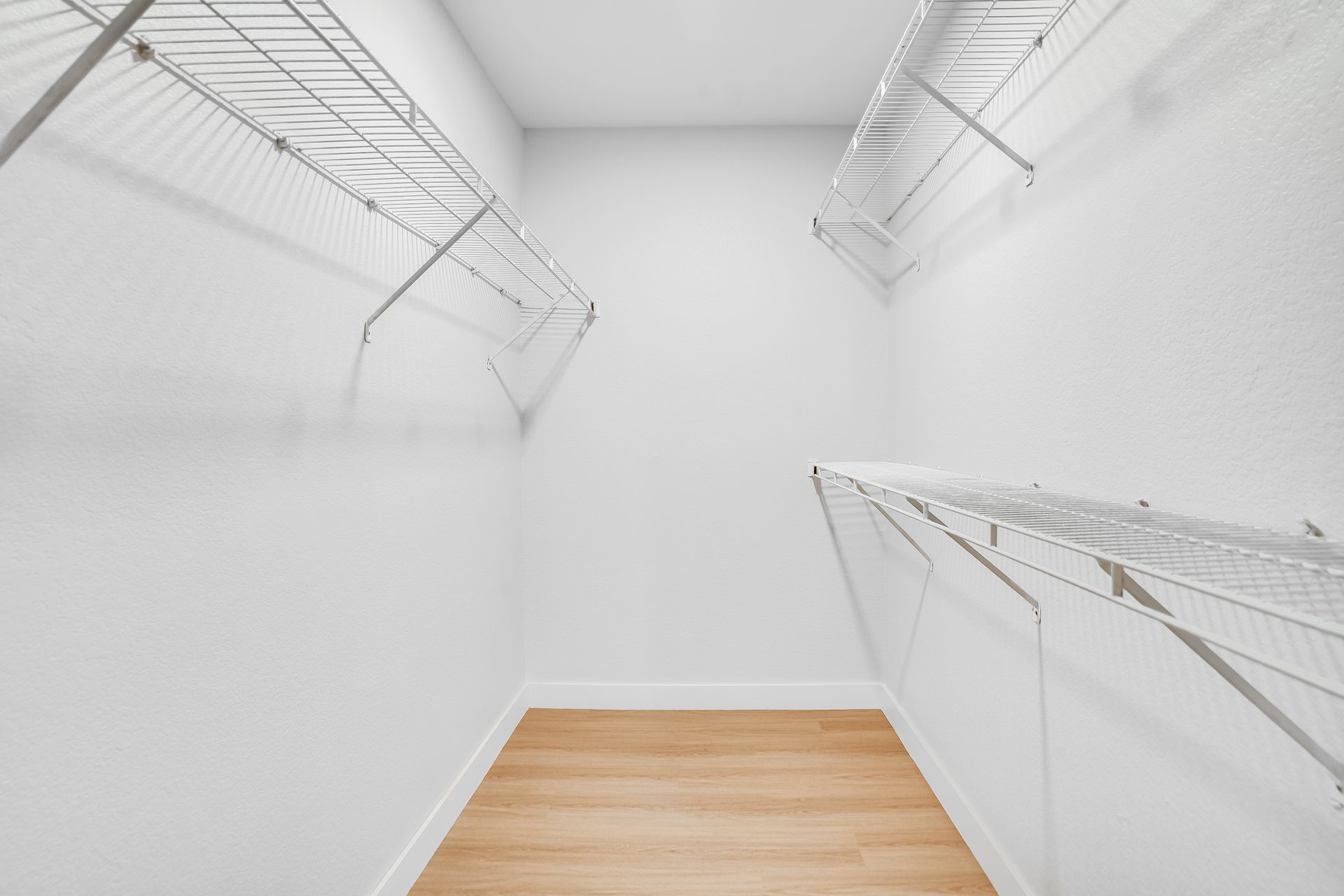 Empty, white-walled closet with wire shelves and light wood floor.