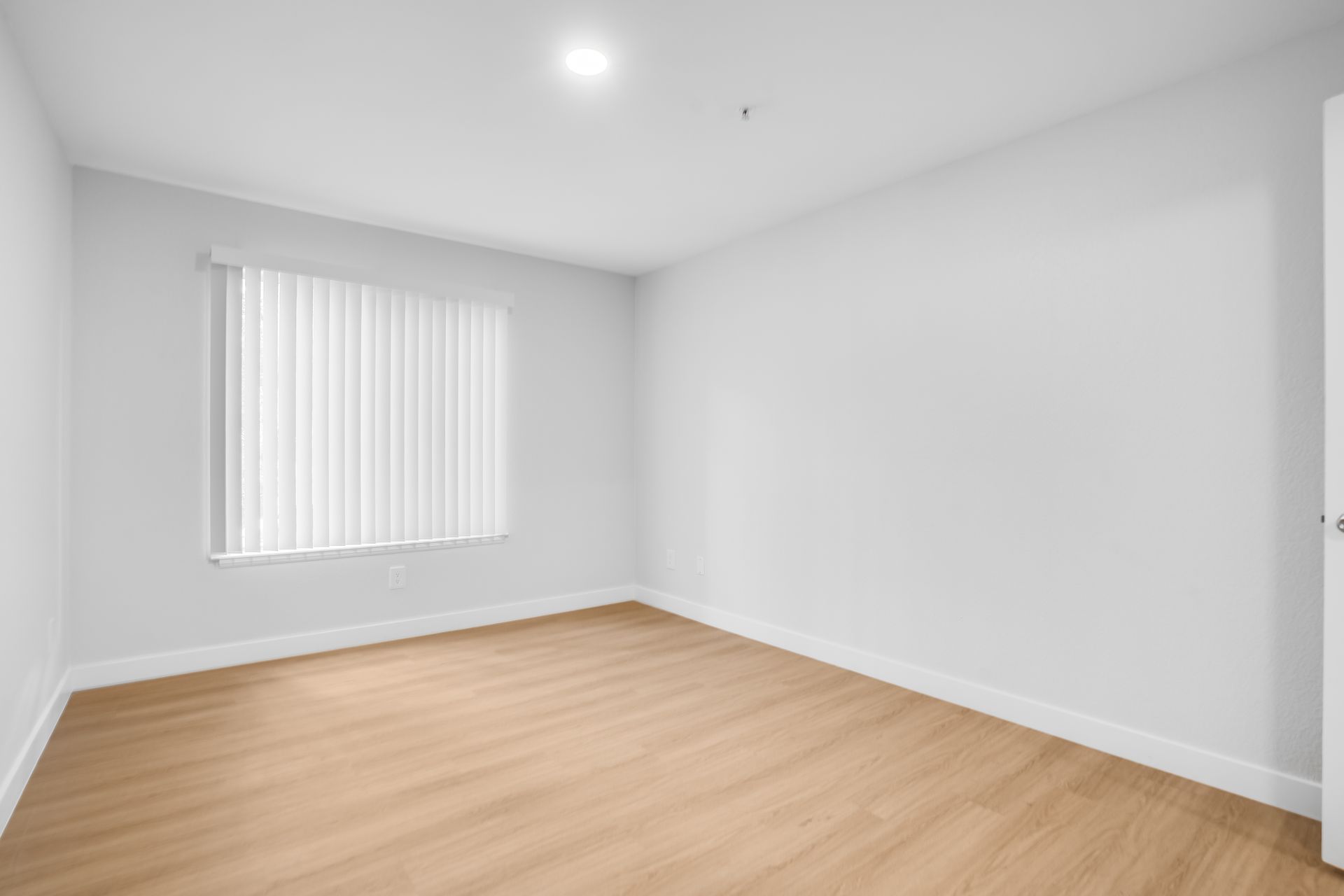 Empty room with light wood floor, white walls, window with blinds.