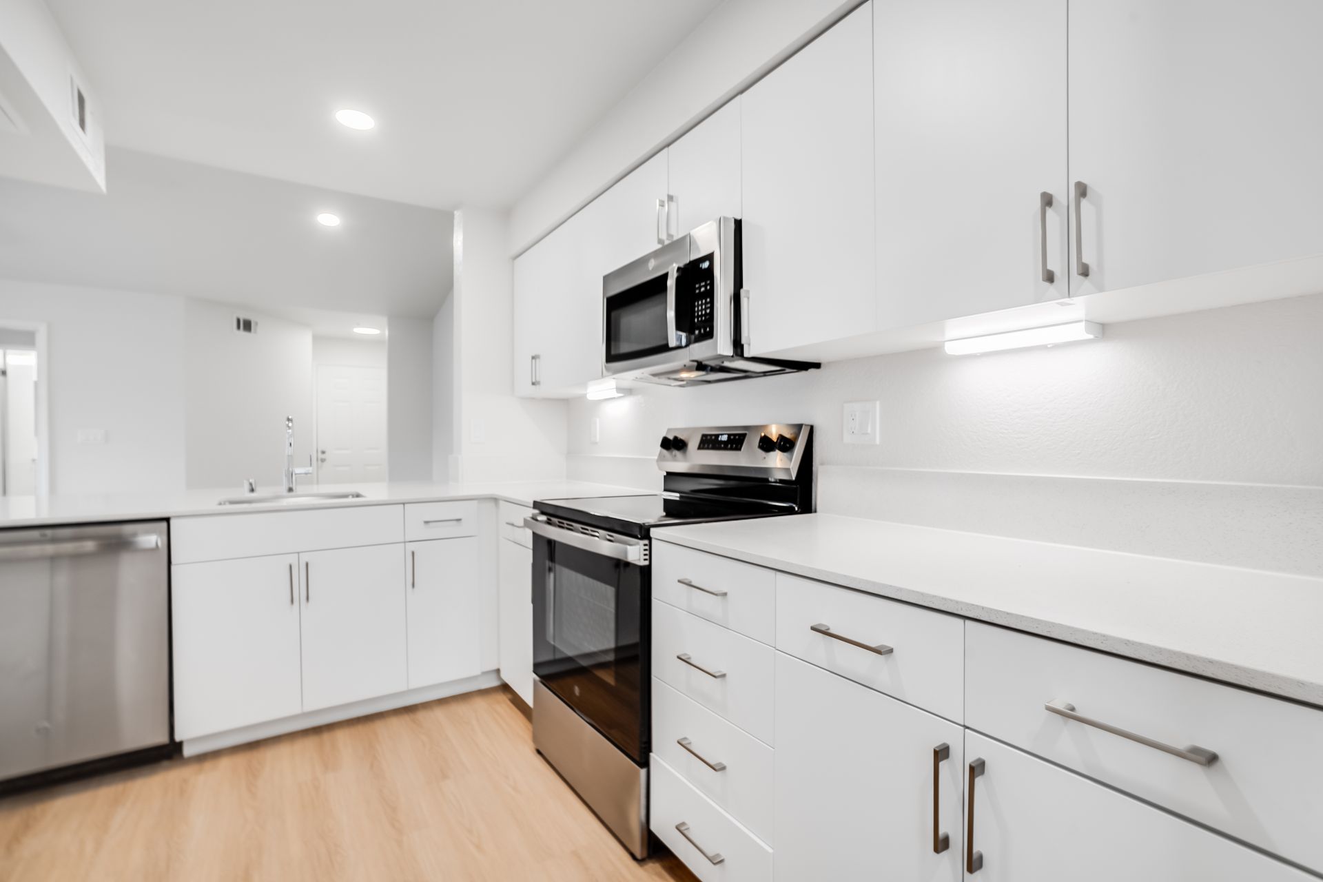 Modern white kitchen with stainless steel appliances and light wood floors.