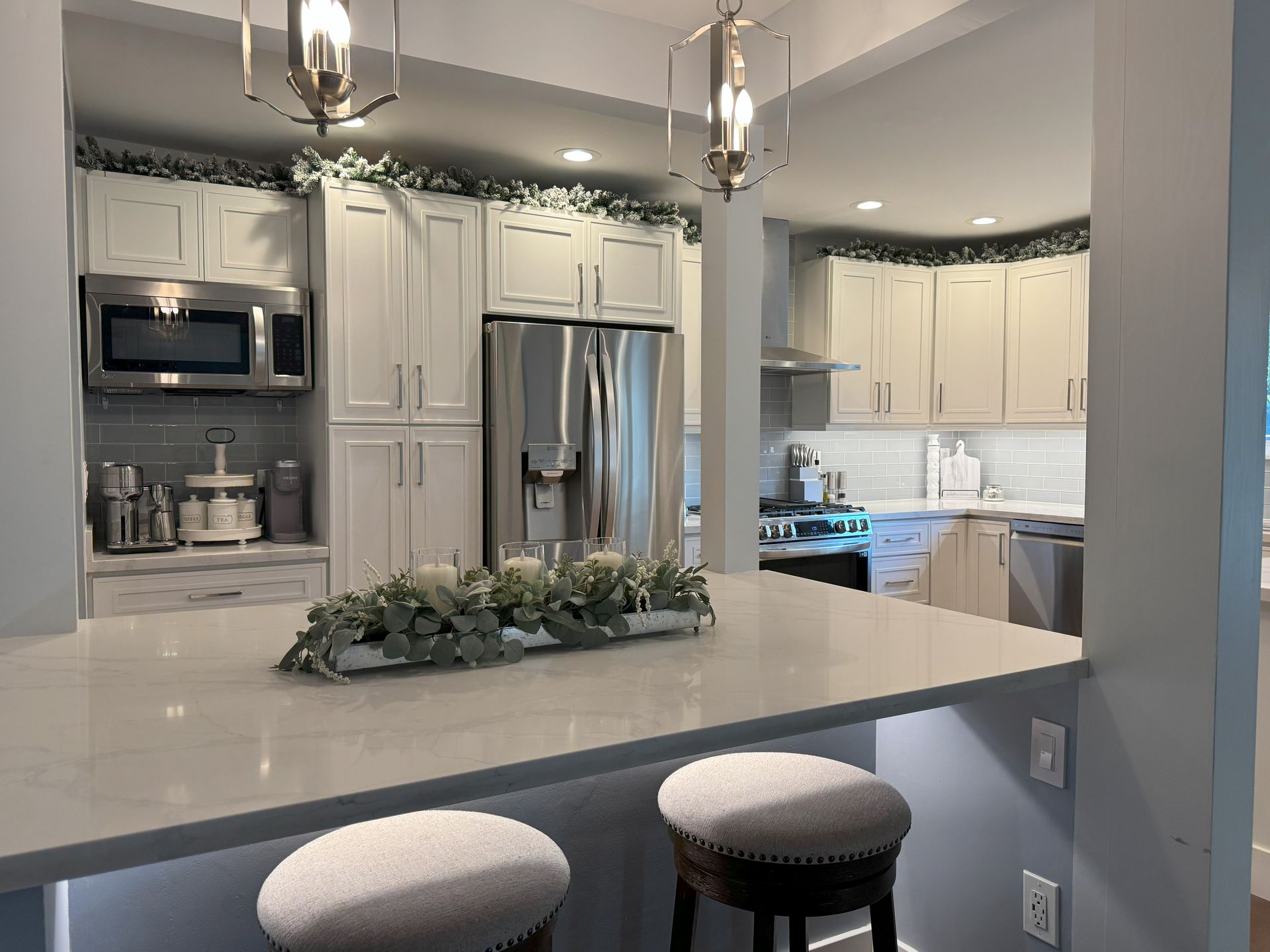 White kitchen with a countertop, cabinets, and stainless steel appliances. Two bar stools are in view.