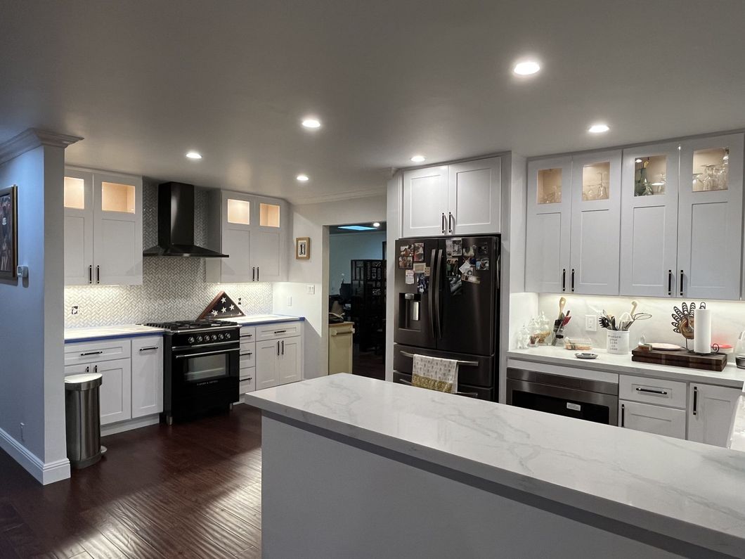 Bright white kitchen with a black stove, refrigerator, and range hood. White countertops and cabinets.