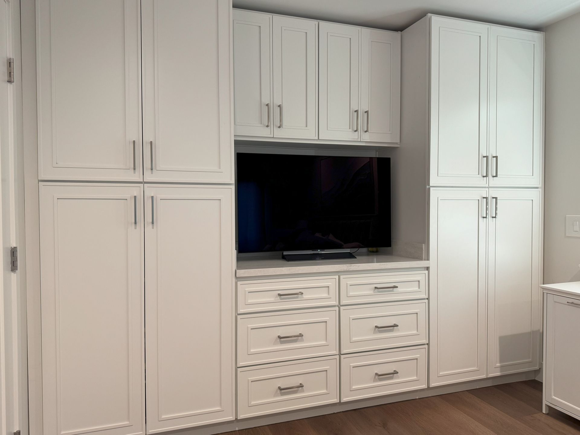 White built-in cabinet system with TV centered above drawers, silver hardware, set against a white wall.