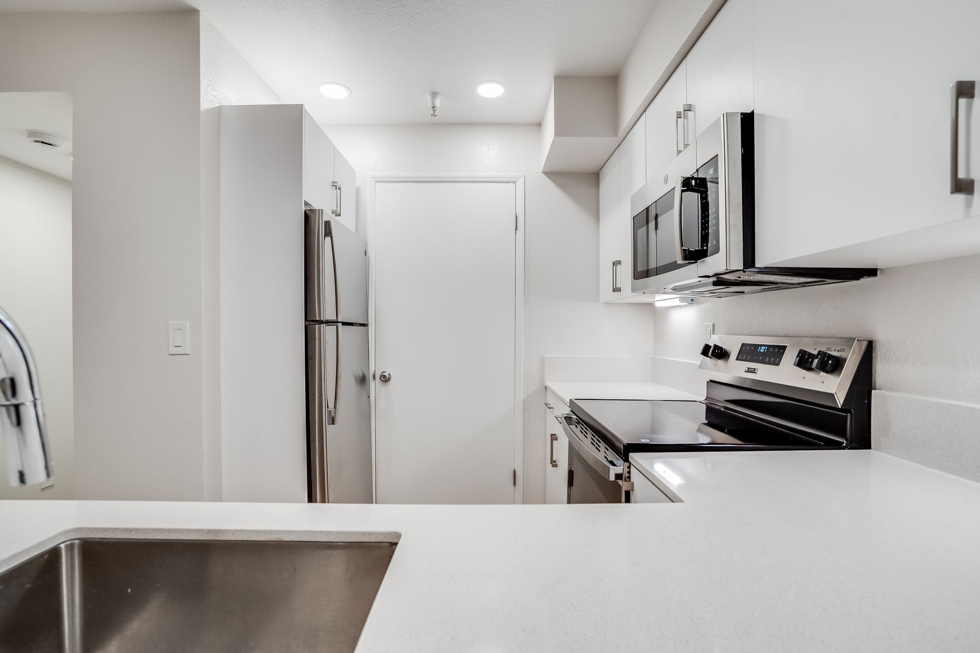 White kitchen with stainless steel appliances, white cabinets, and countertop.