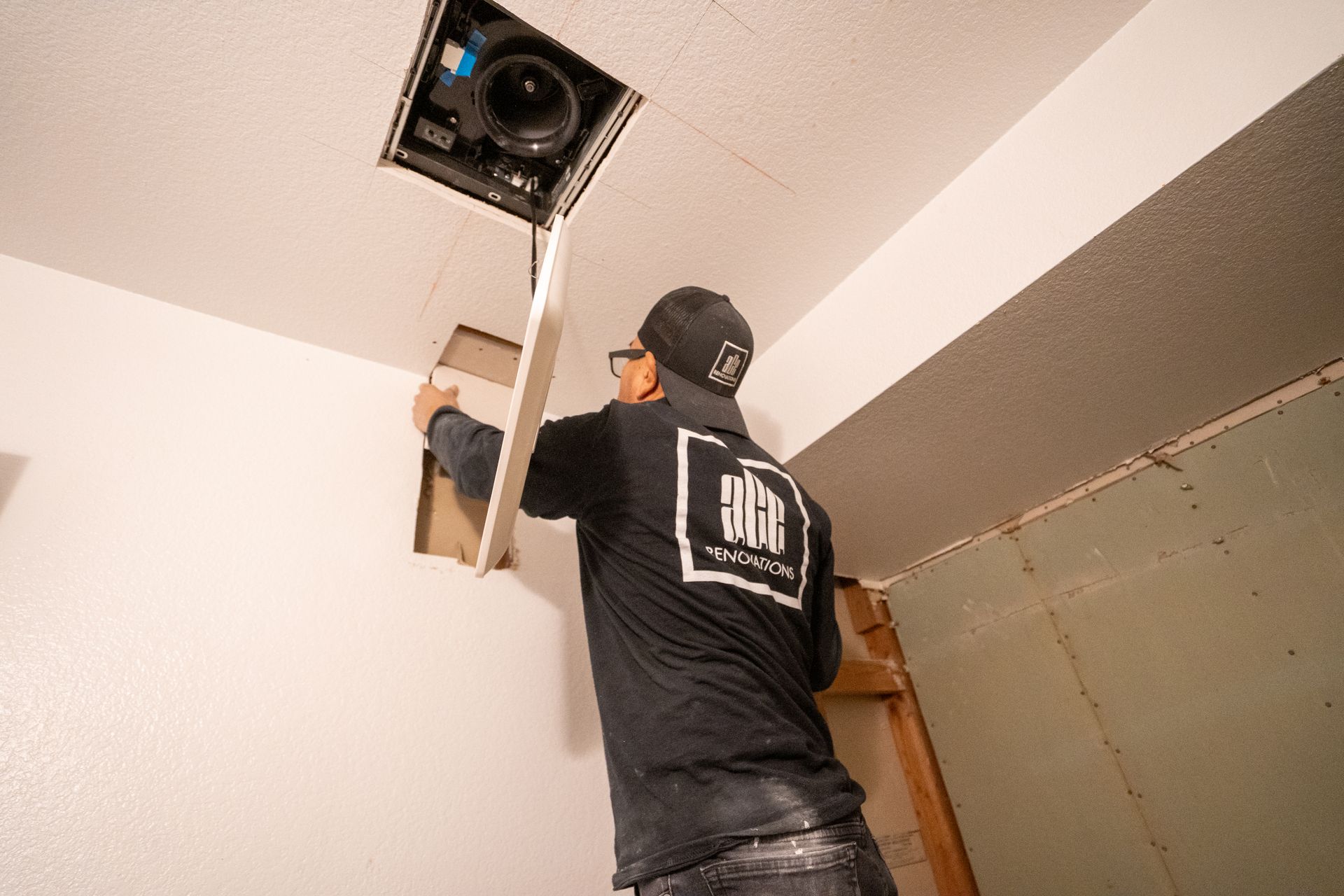 Person in black shirt installing a ceiling vent in a room with exposed drywall.