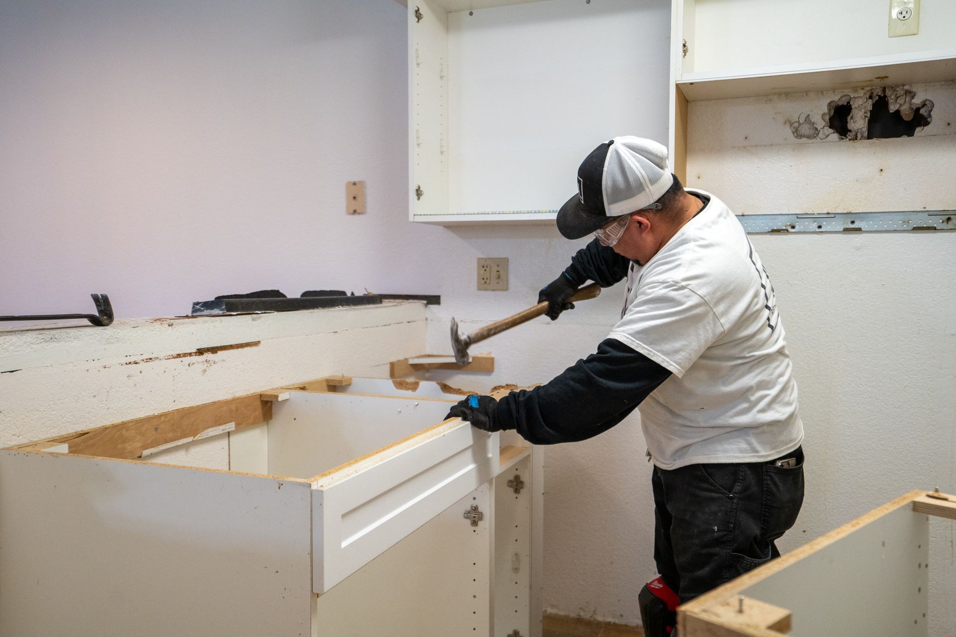 Person in a kitchen removing cabinets with a hammer