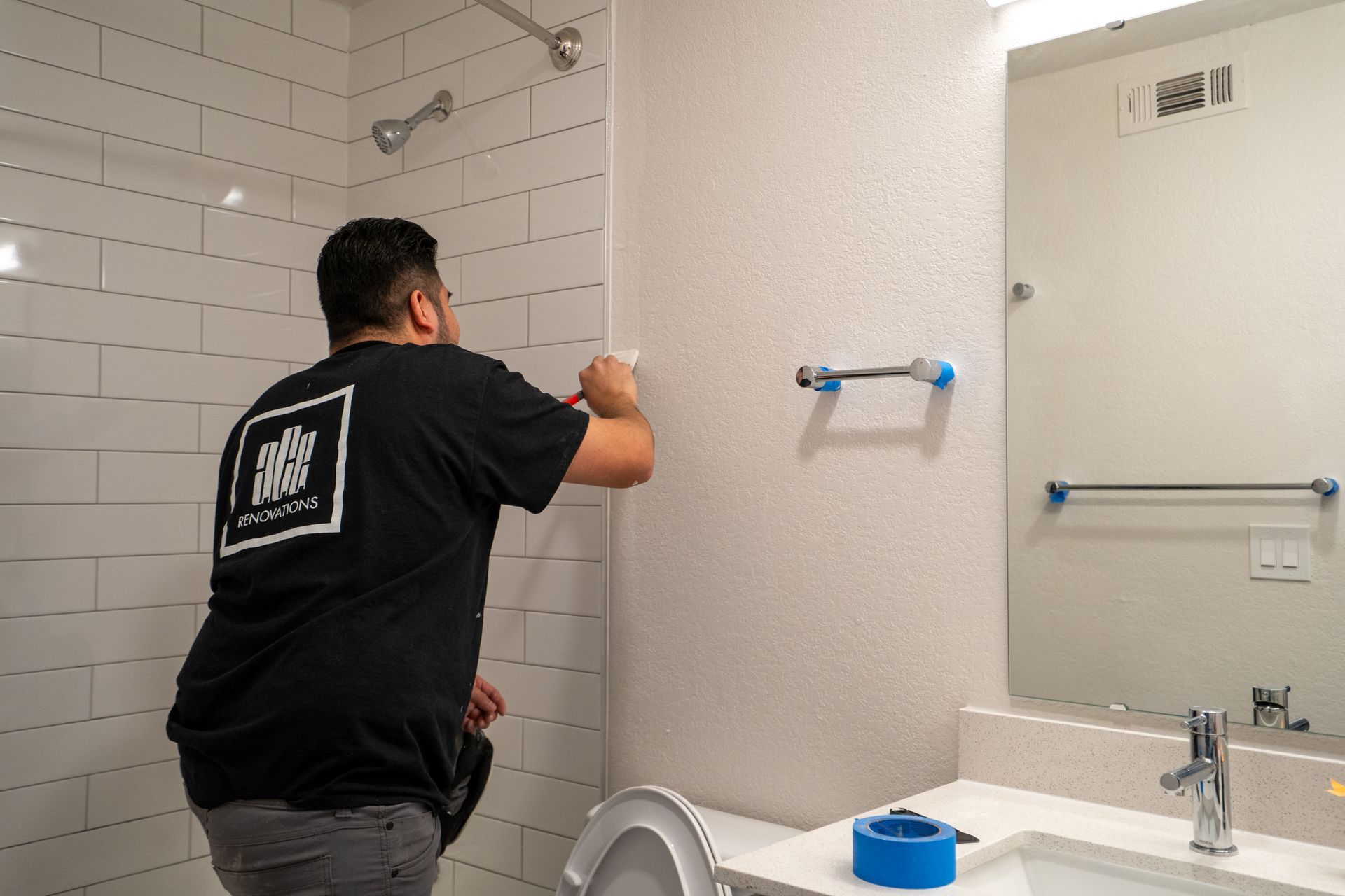 Person in black shirt painting wall in bathroom. 