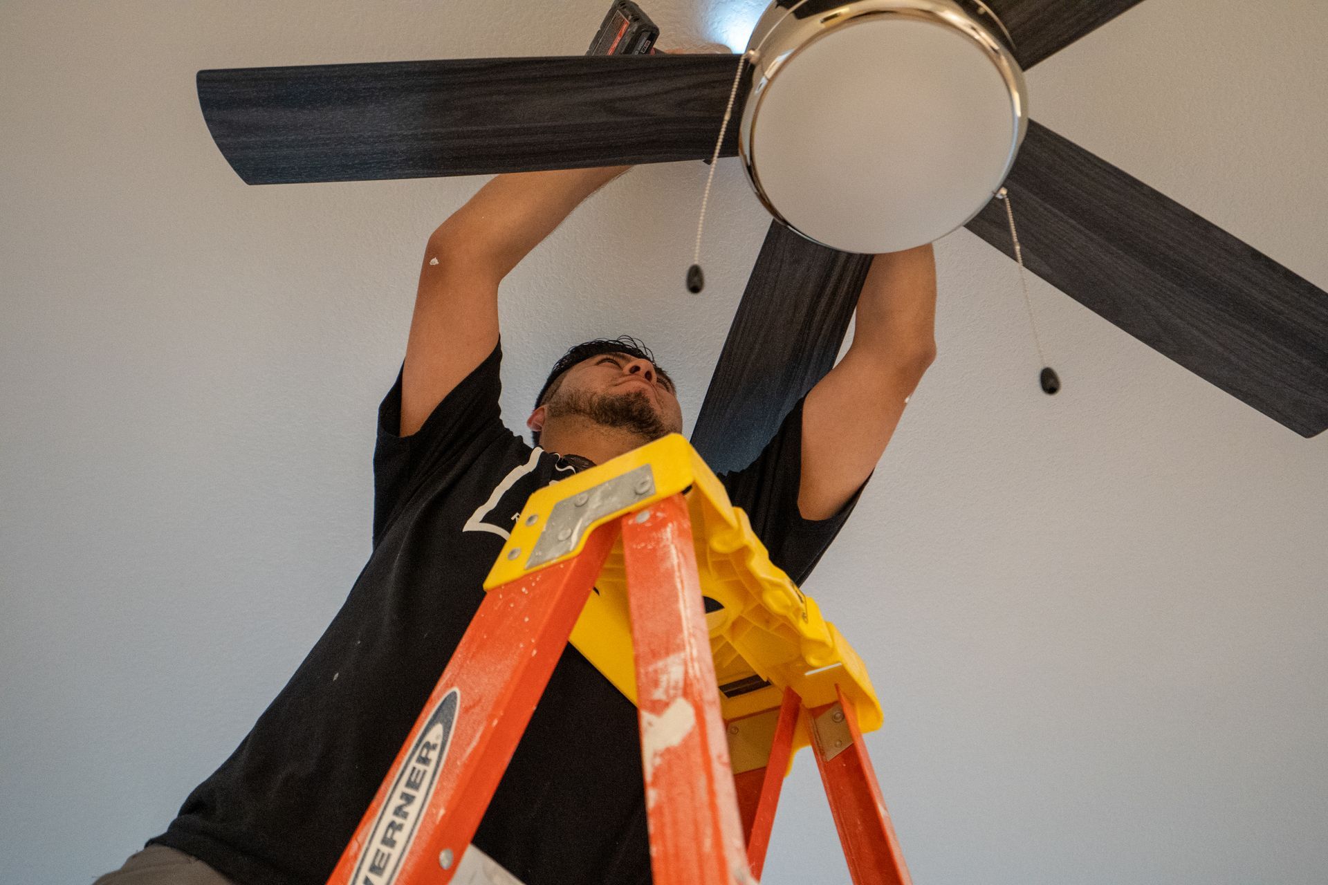 Man on a ladder installing a ceiling fan.