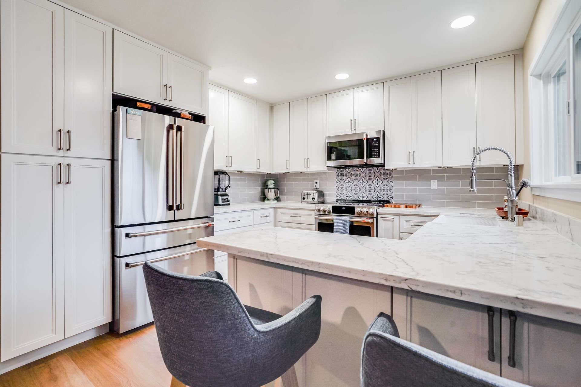 White kitchen with stainless steel appliances, marble countertops, and gray bar stools.
