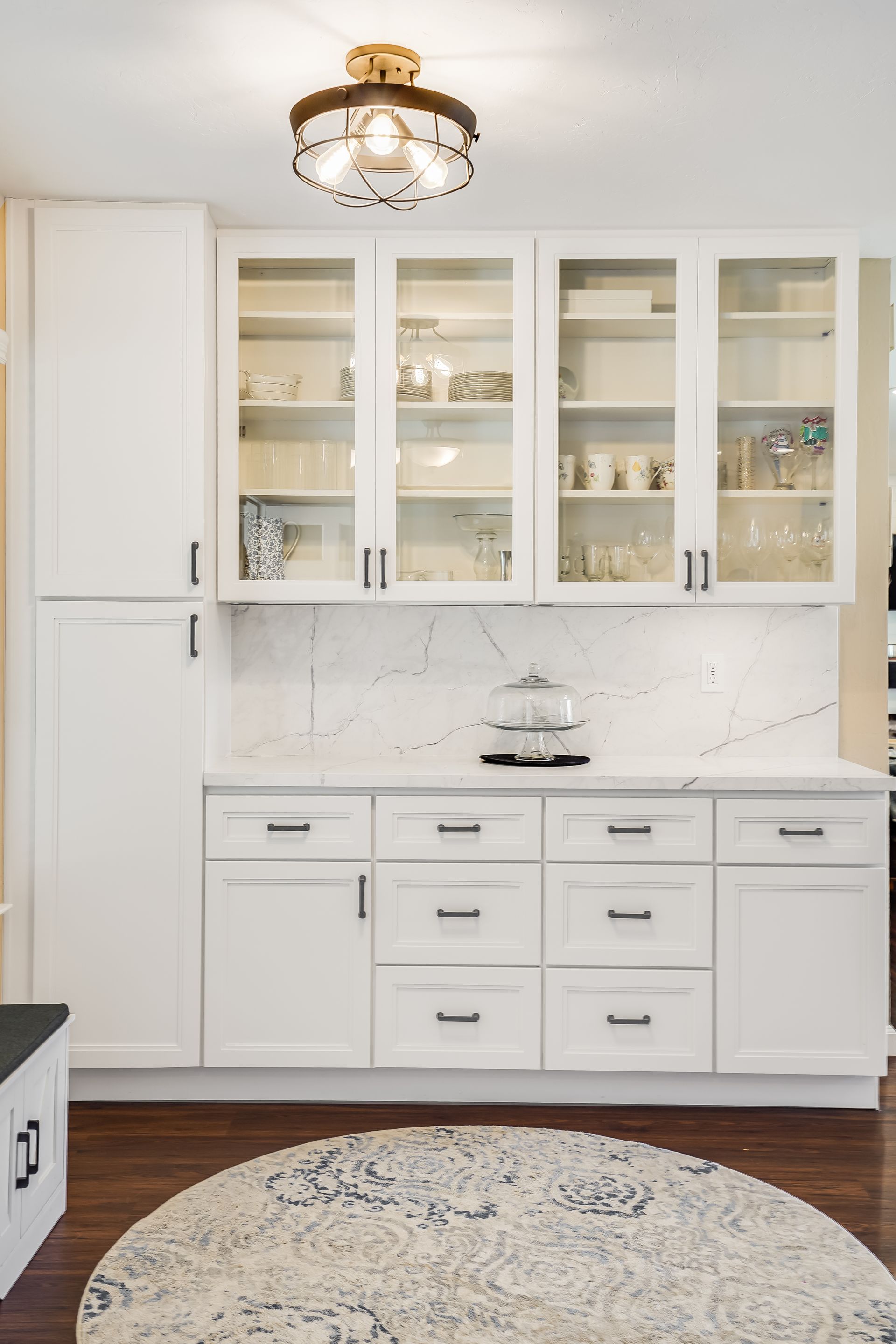 White kitchen cabinets with glass-front uppers, drawers, and countertop with marble backsplash.