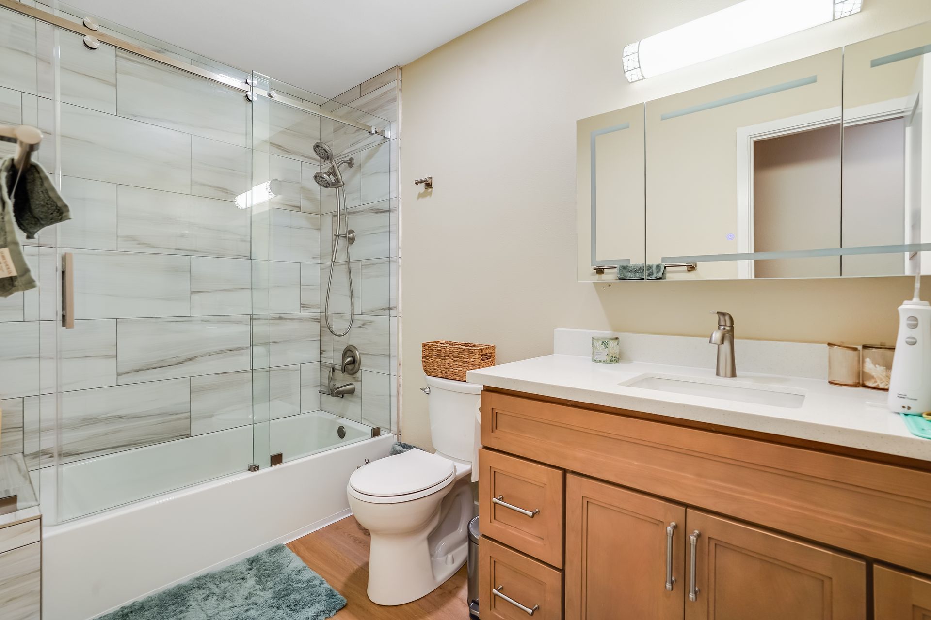 Bathroom with a bathtub, toilet, sink, and wood cabinetry. White and gray tiled shower.