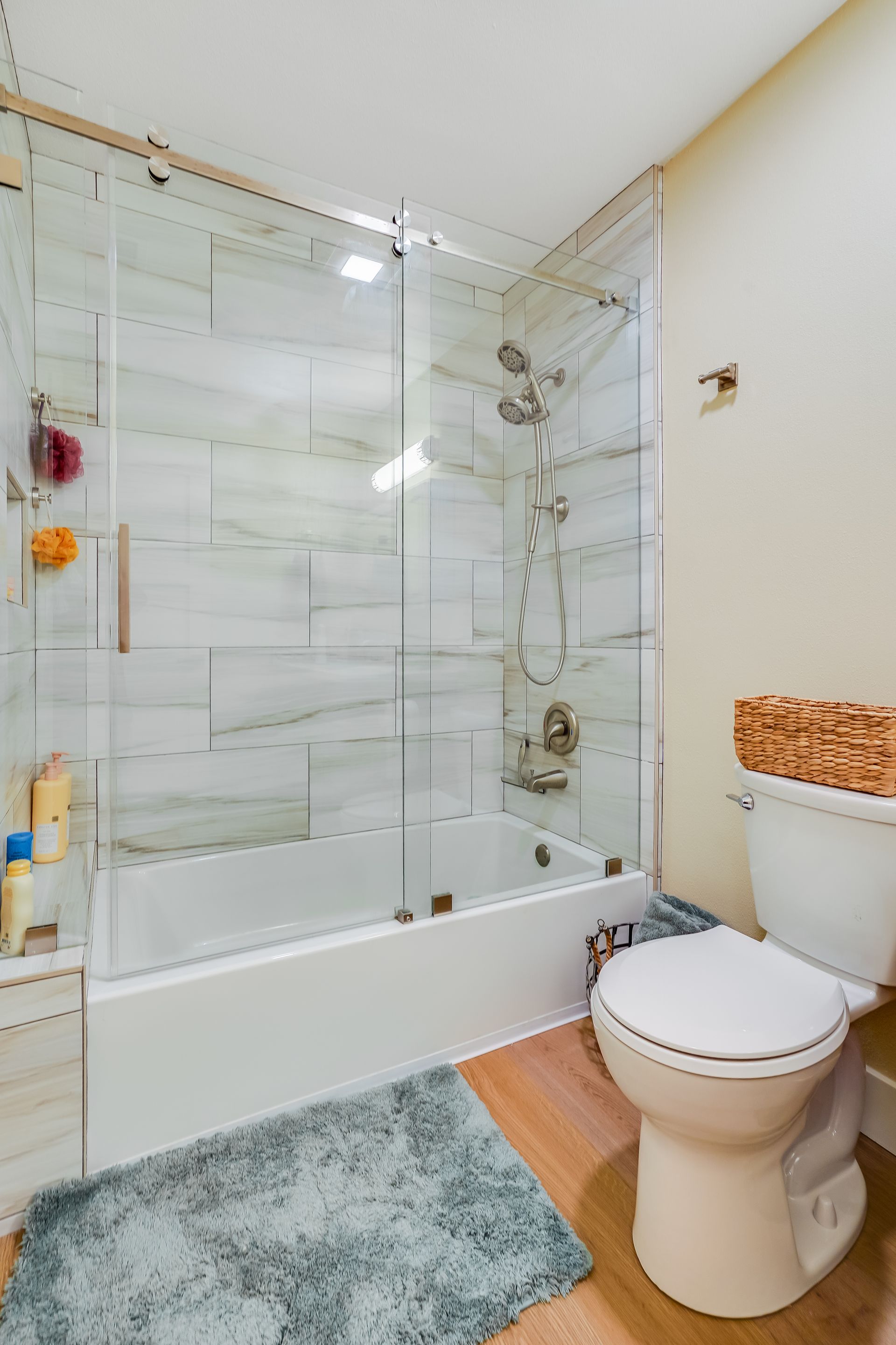 Bathroom with white tub, glass shower enclosure, and white toilet on wood floor.
