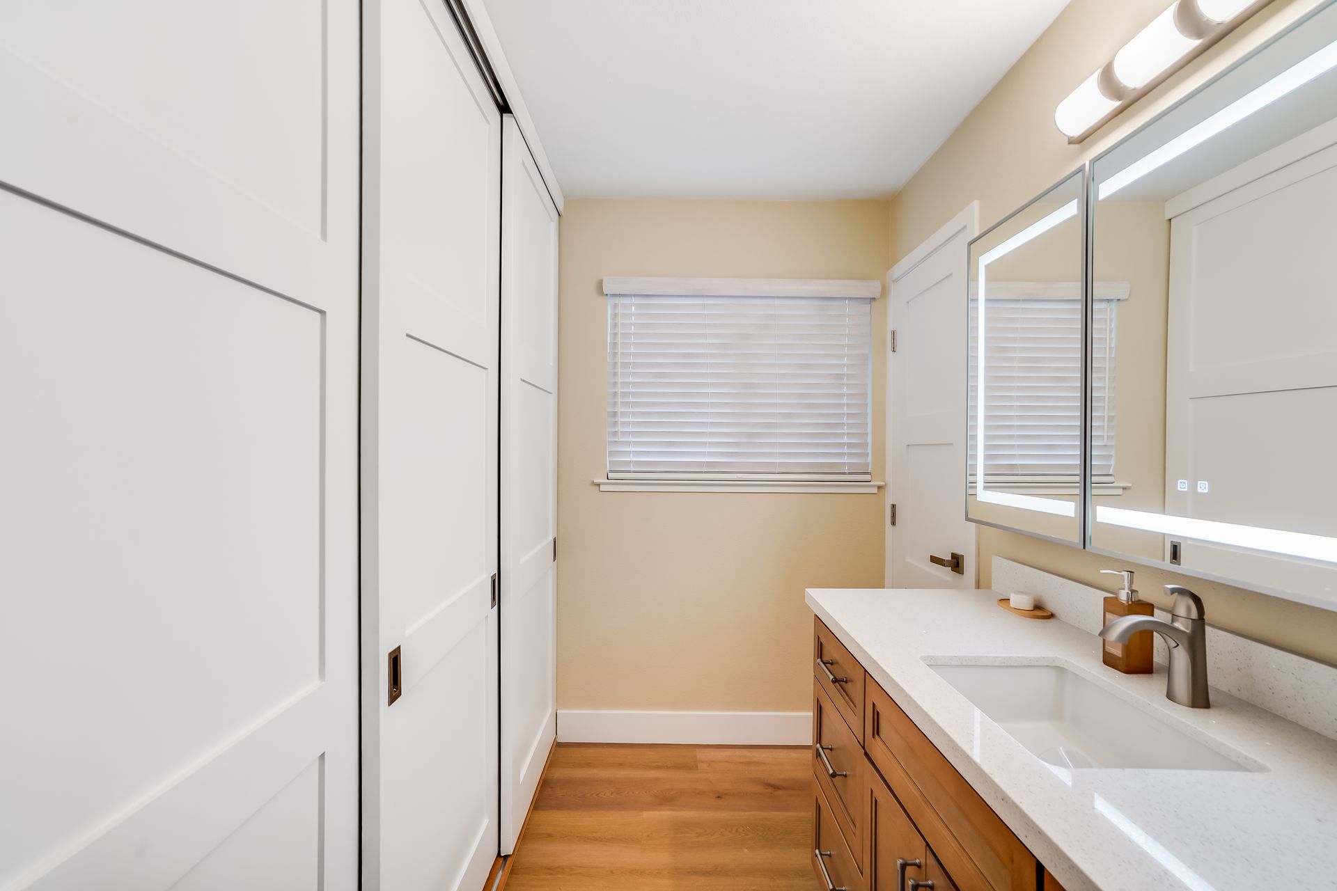 Bathroom with white cabinets, wood vanity, and a window with blinds.