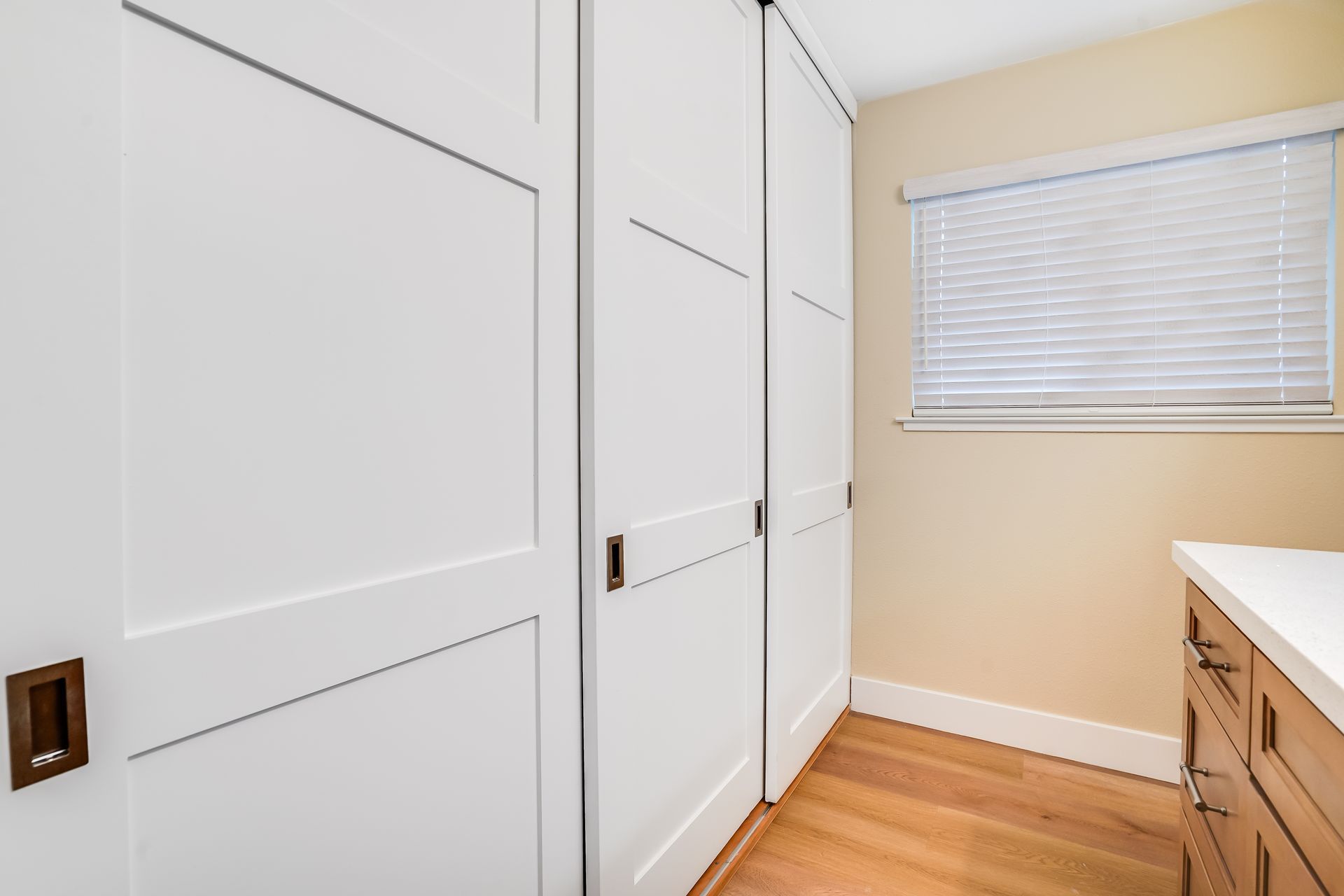 White closet doors, wooden floor, and a window with blinds.