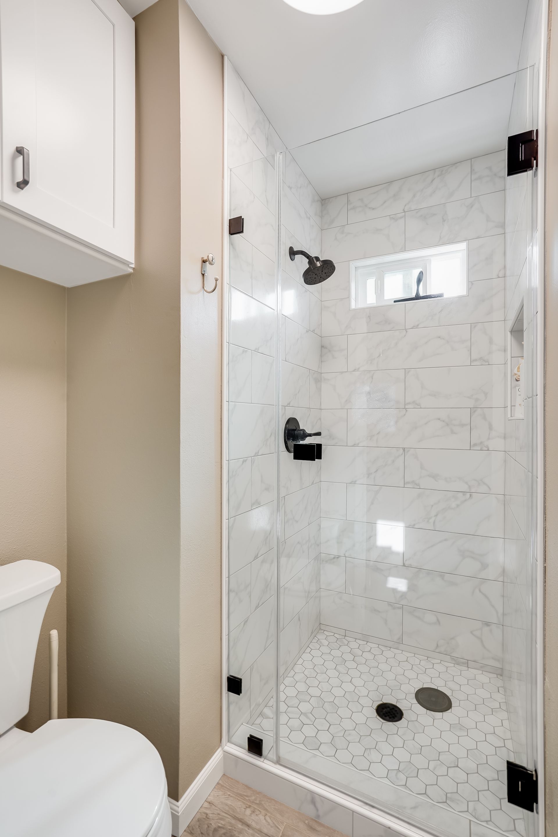 Small bathroom with a white-tiled shower, glass door, and black fixtures.