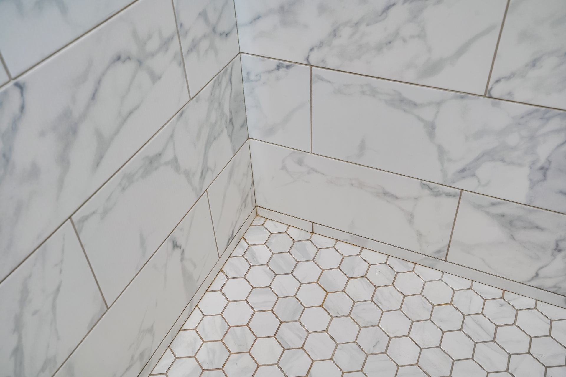 White marble-patterned tile shower corner with hexagon tile floor.
