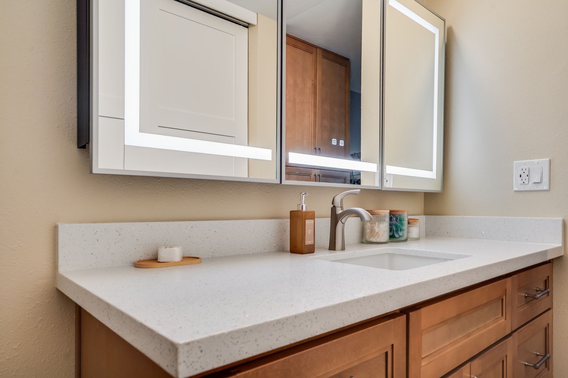 Bathroom vanity with white countertop, wood cabinets, and lighted mirror.