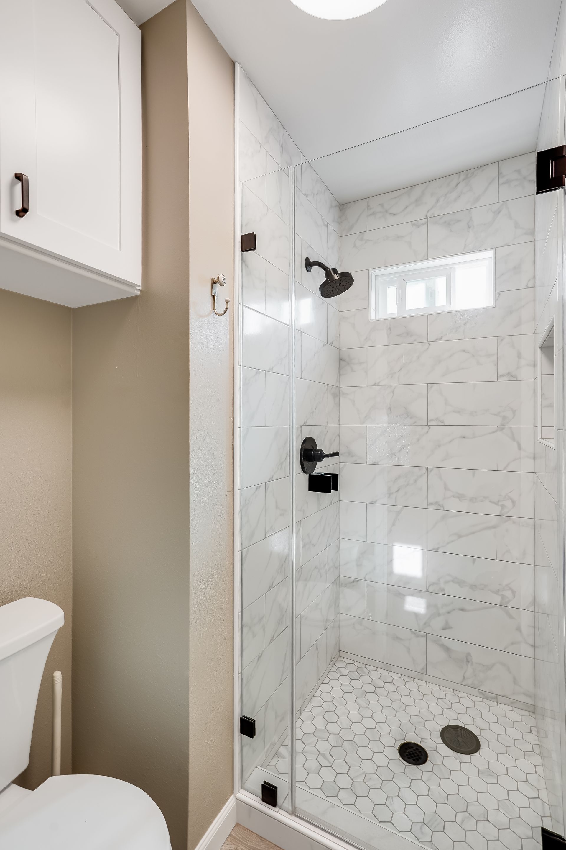 Bathroom with white toilet, marble-tiled shower, and glass door. Black hardware.