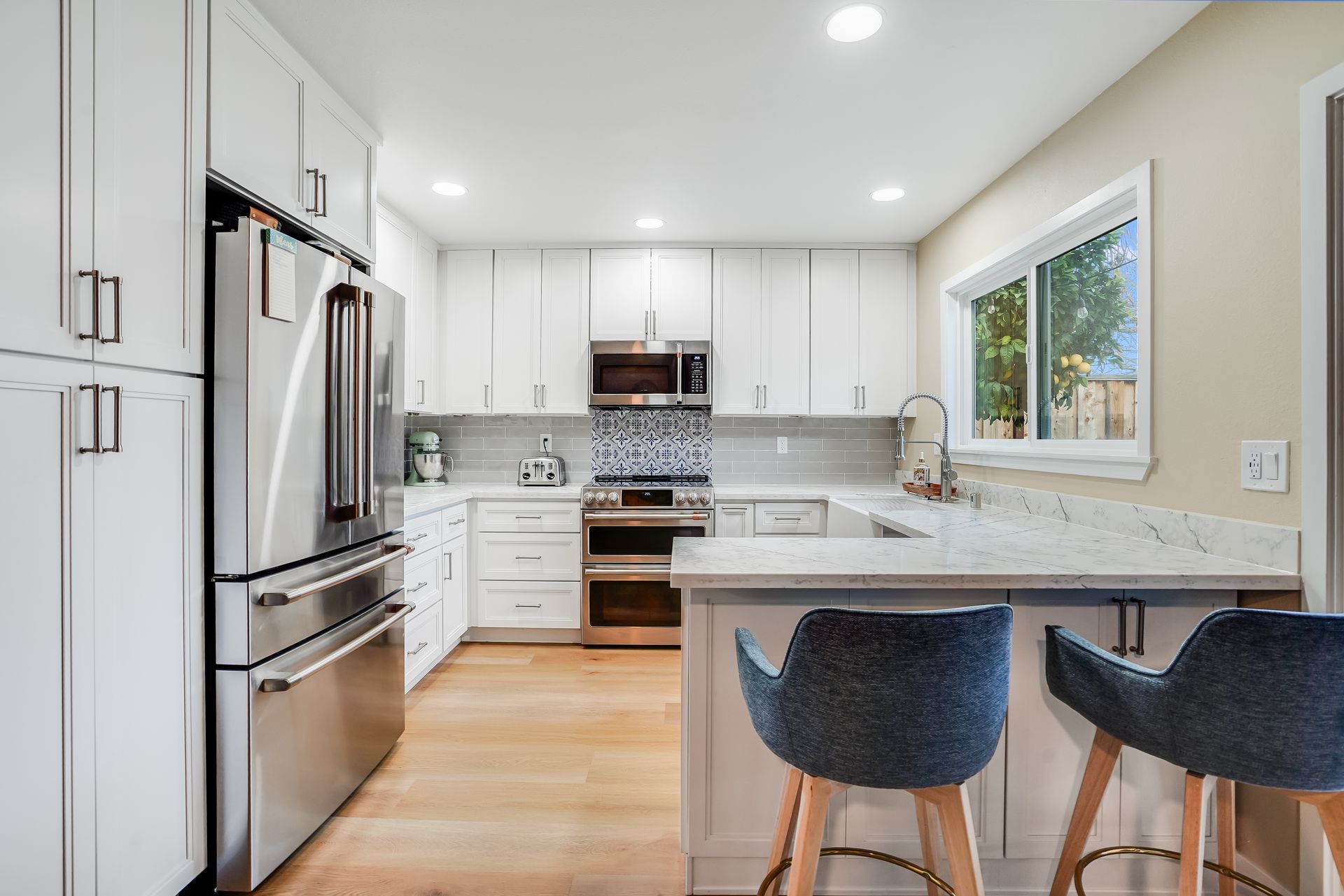 Bright kitchen with white cabinets, stainless steel appliances, and a breakfast bar with blue stools.