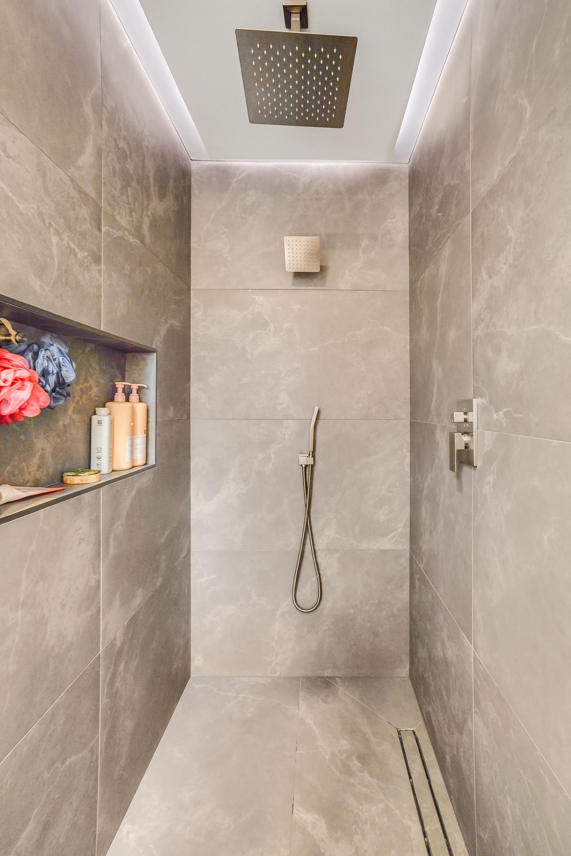 Modern gray tiled shower with built-in shelf, rainfall showerhead, and handheld shower.