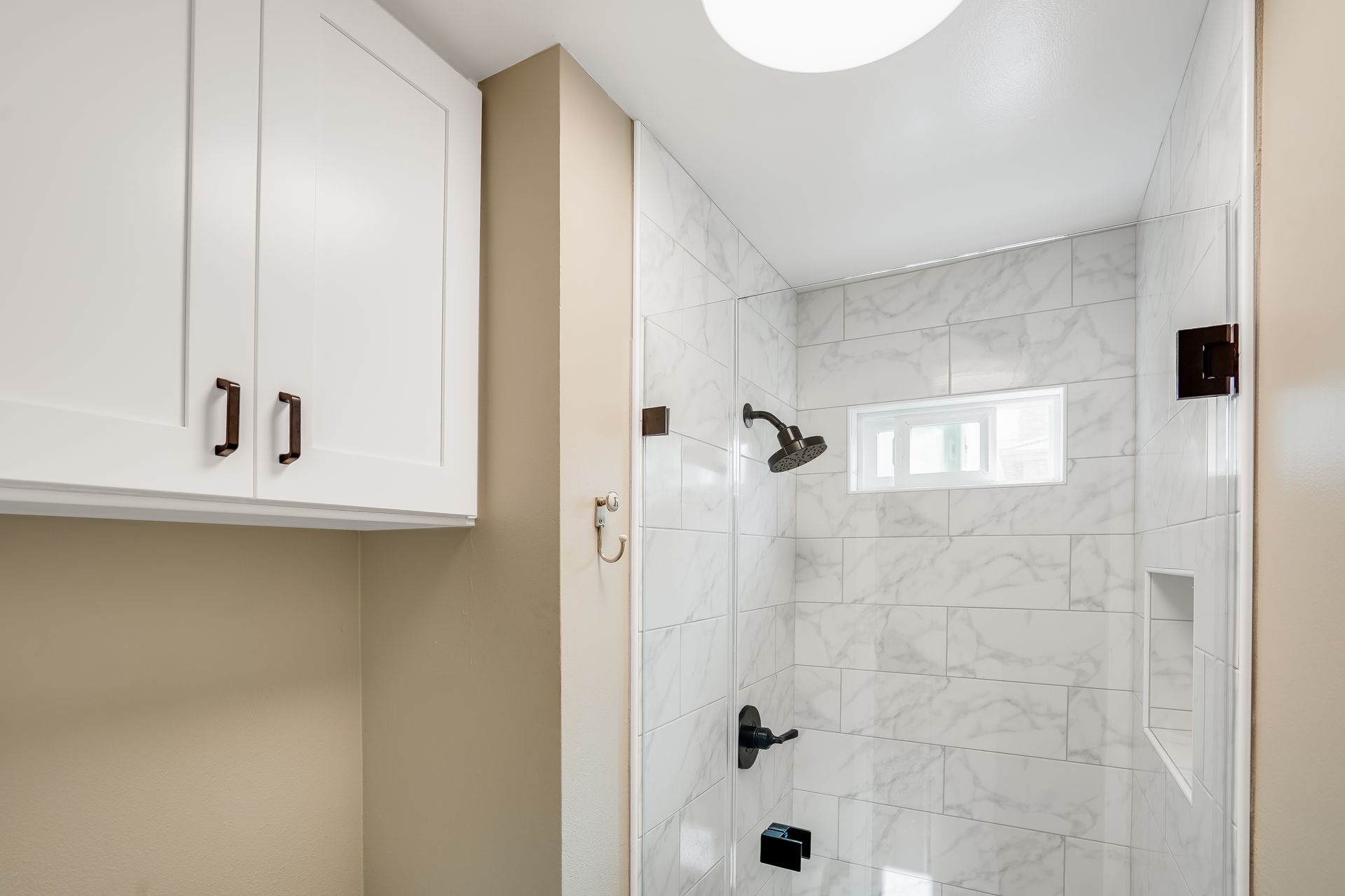 Bathroom with white marble shower, glass door, dark fixtures, and white cabinets.