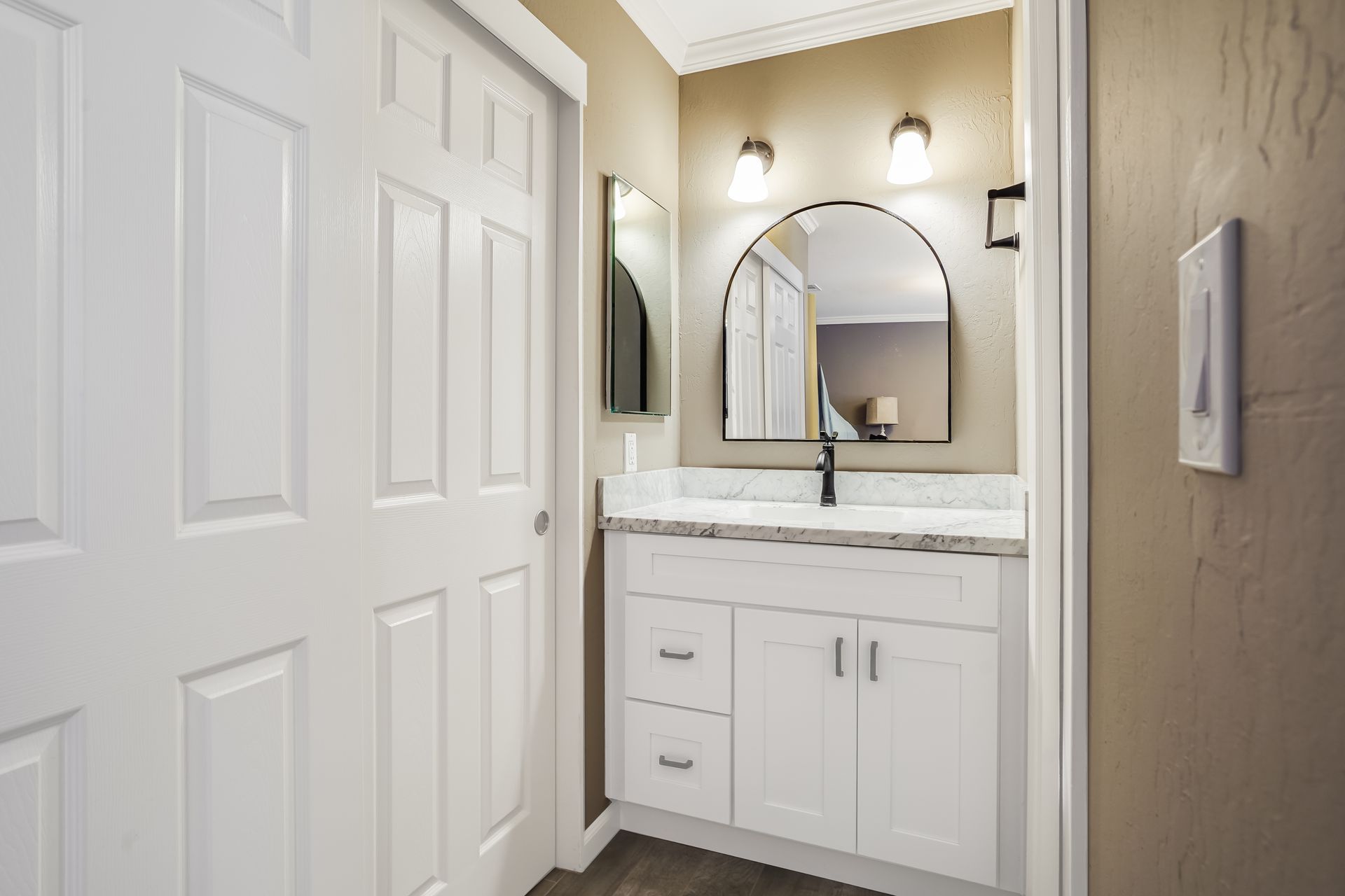 White bathroom vanity with arched mirror, two sconces, and closed door.