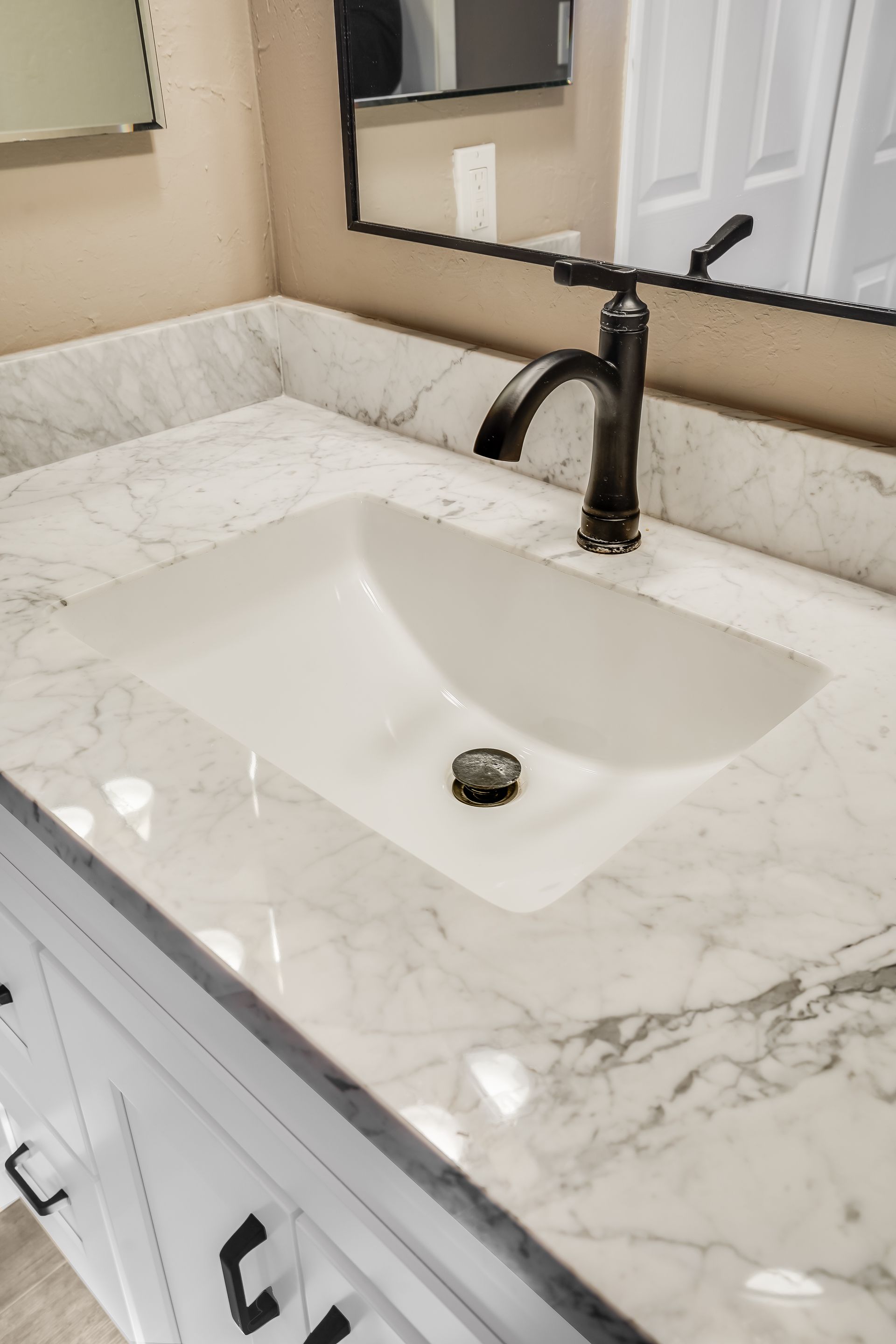 White bathroom sink on marble countertop, black faucet, mirror.