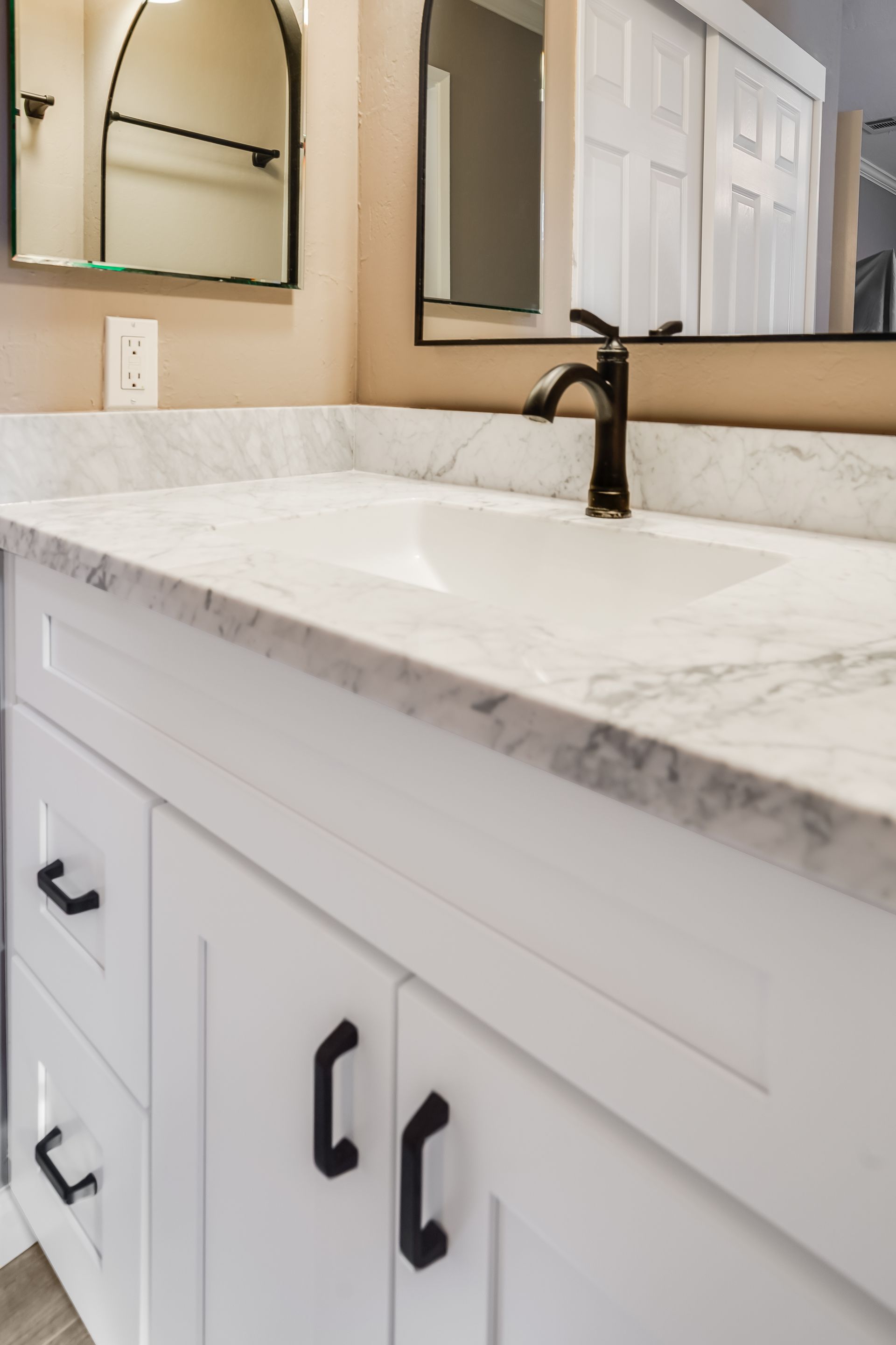 White bathroom vanity with marble countertop, black faucet, and cabinet hardware.
