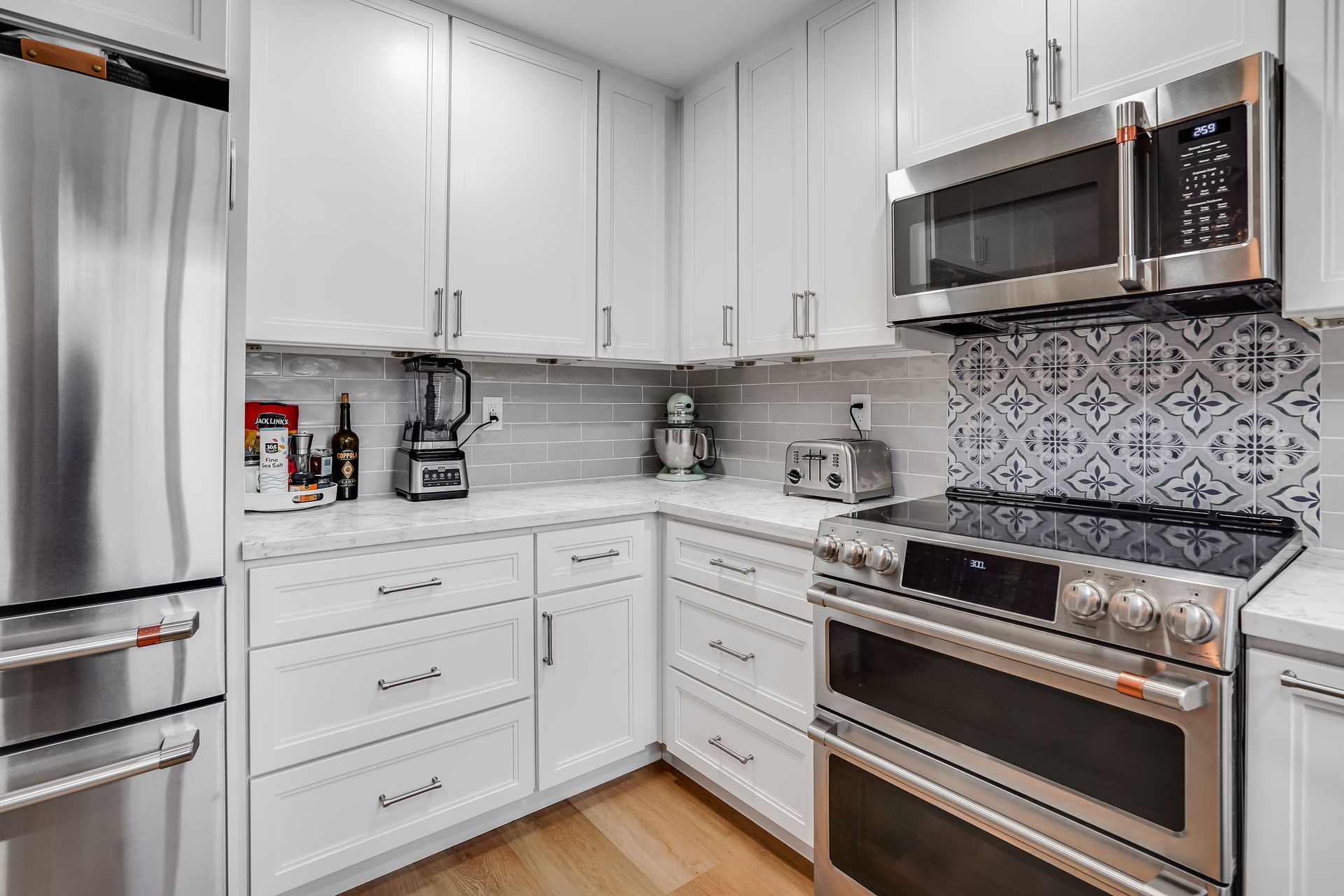 White kitchen with stainless steel appliances, white cabinets, and patterned backsplash.