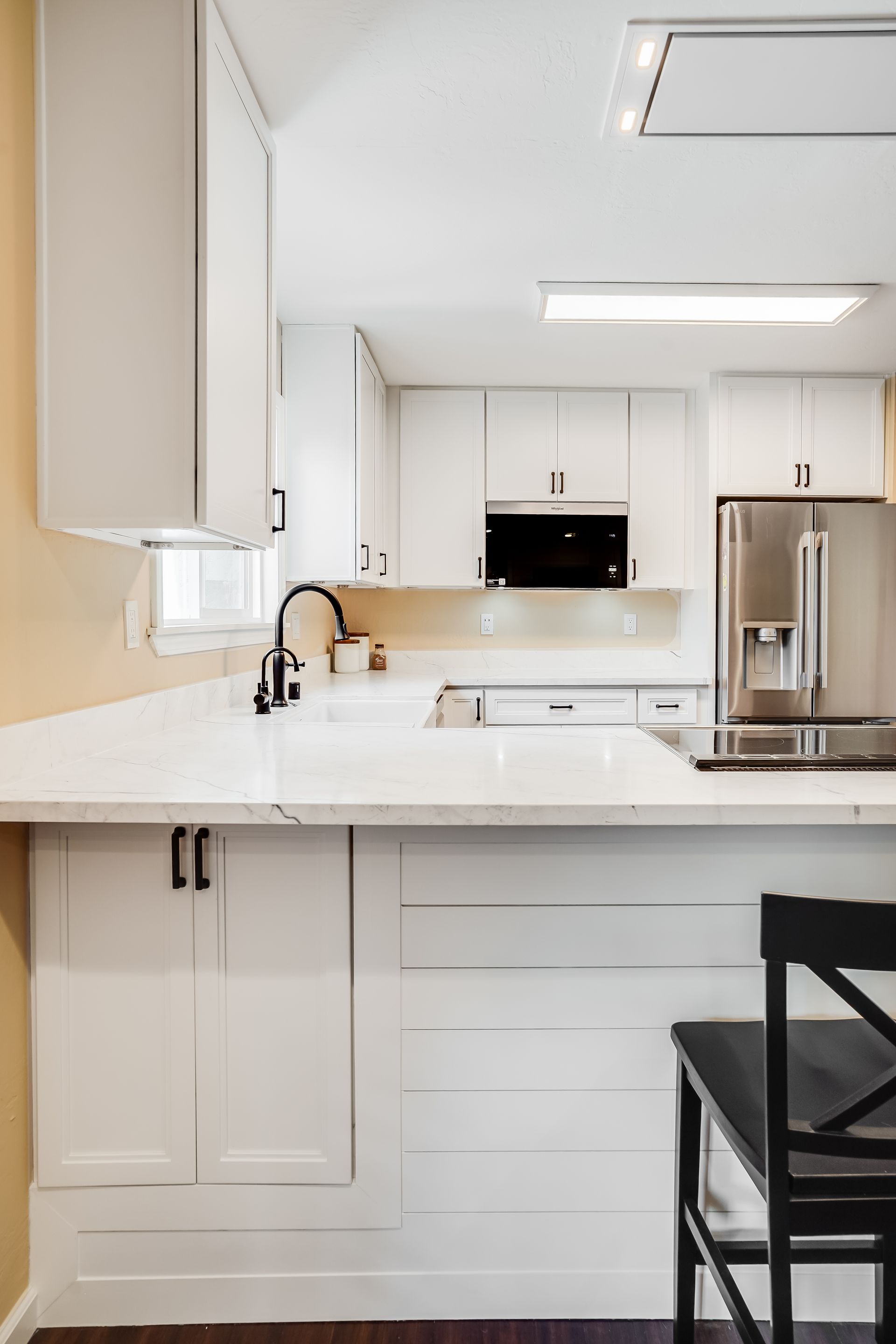 White kitchen with white countertops and cabinets, black hardware and faucet, and stainless steel appliances.